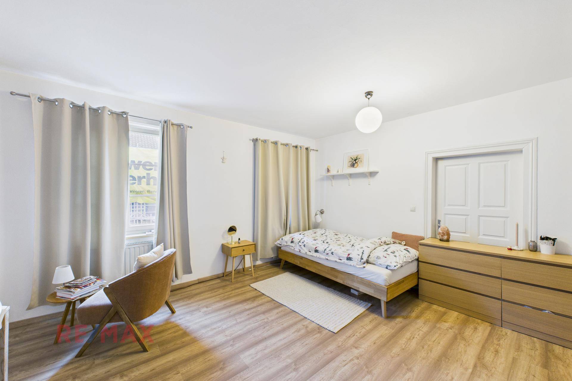 Helles Schlafzimmer mit Einzelbett, Kommode und Laminatboden, gemütlich eingerichtet.