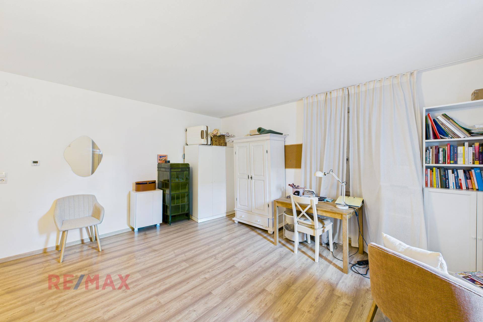 Großes Zimmer mit Kachelofen, Schrank und Schreibtisch, ideal als Wohn- oder Arbeitsbereich.