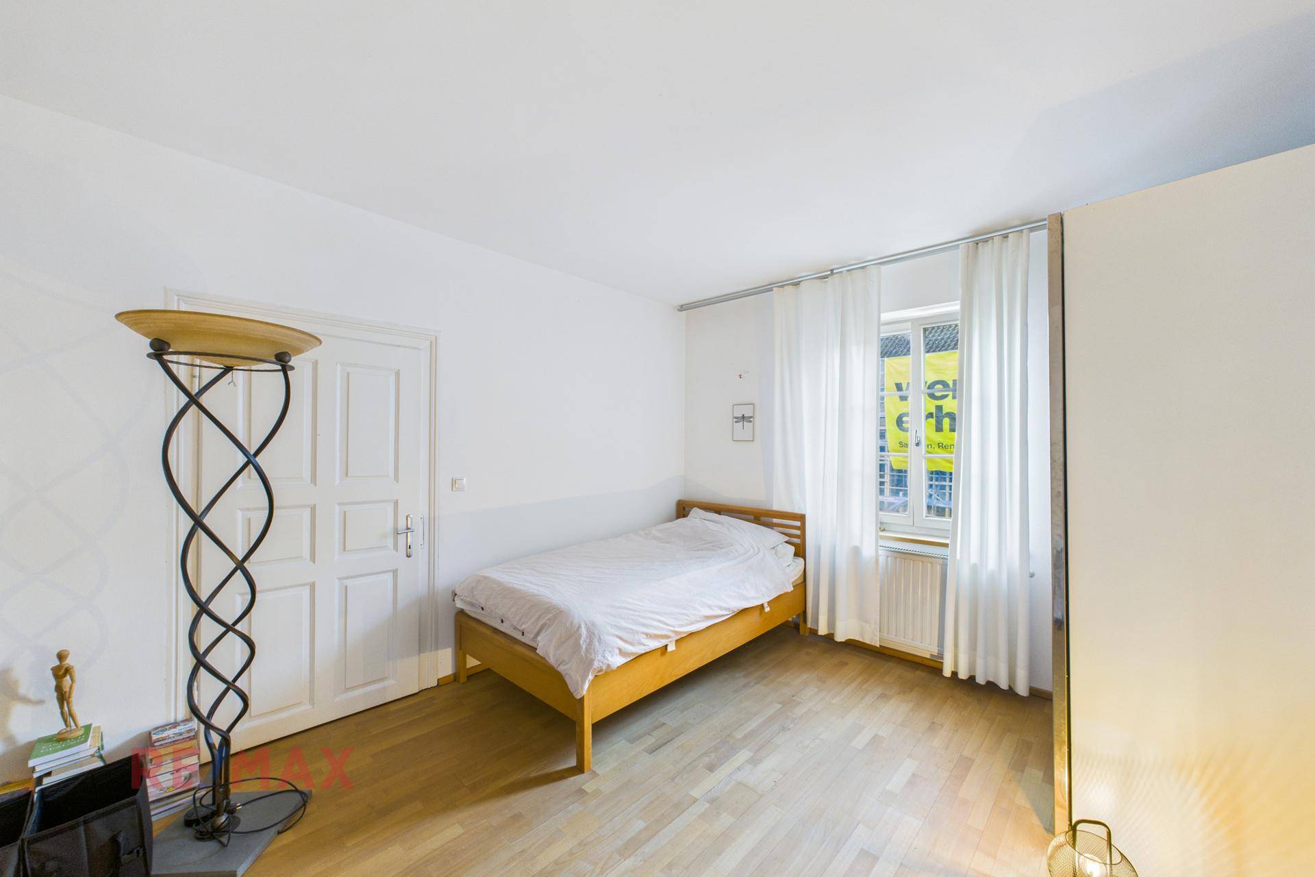 Helles Schlafzimmer mit Einzelbett, Kleiderschrank und Parkettboden, mit Blick nach draußen.