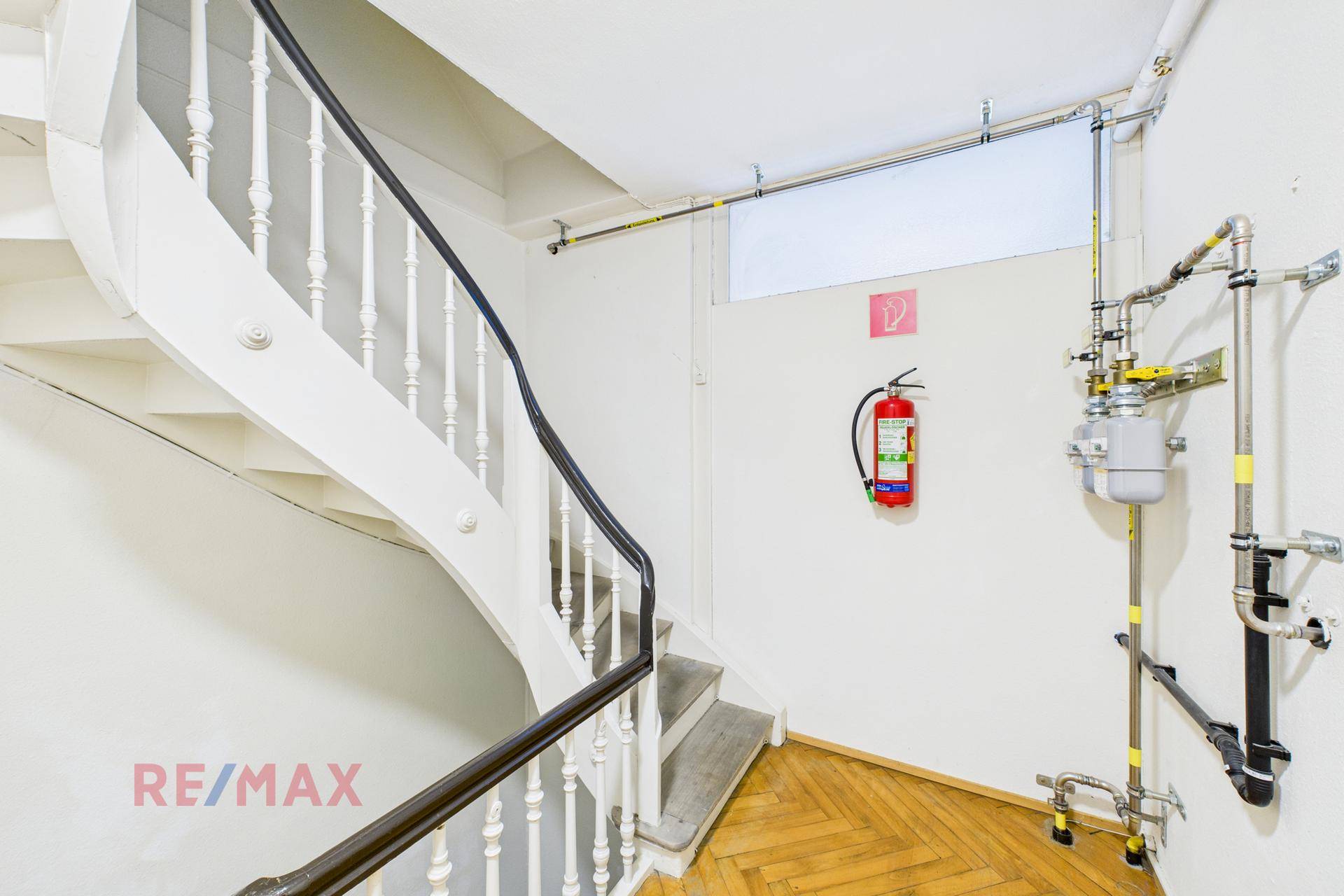 Treppenhaus mit sichtbaren Rohren und Feuerlöscher, typisch für ein älteres Gebäude.