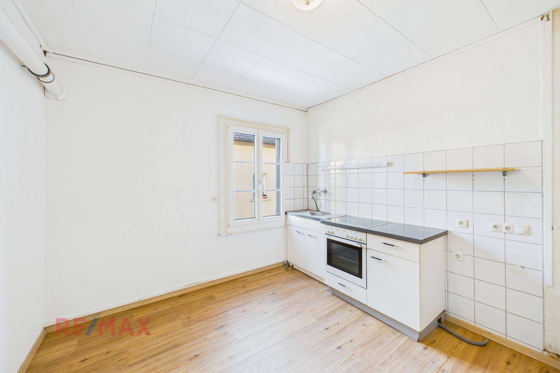 Einfache Küche mit weißen Schränken, Spüle und Herd, bereit zur Modernisierung.