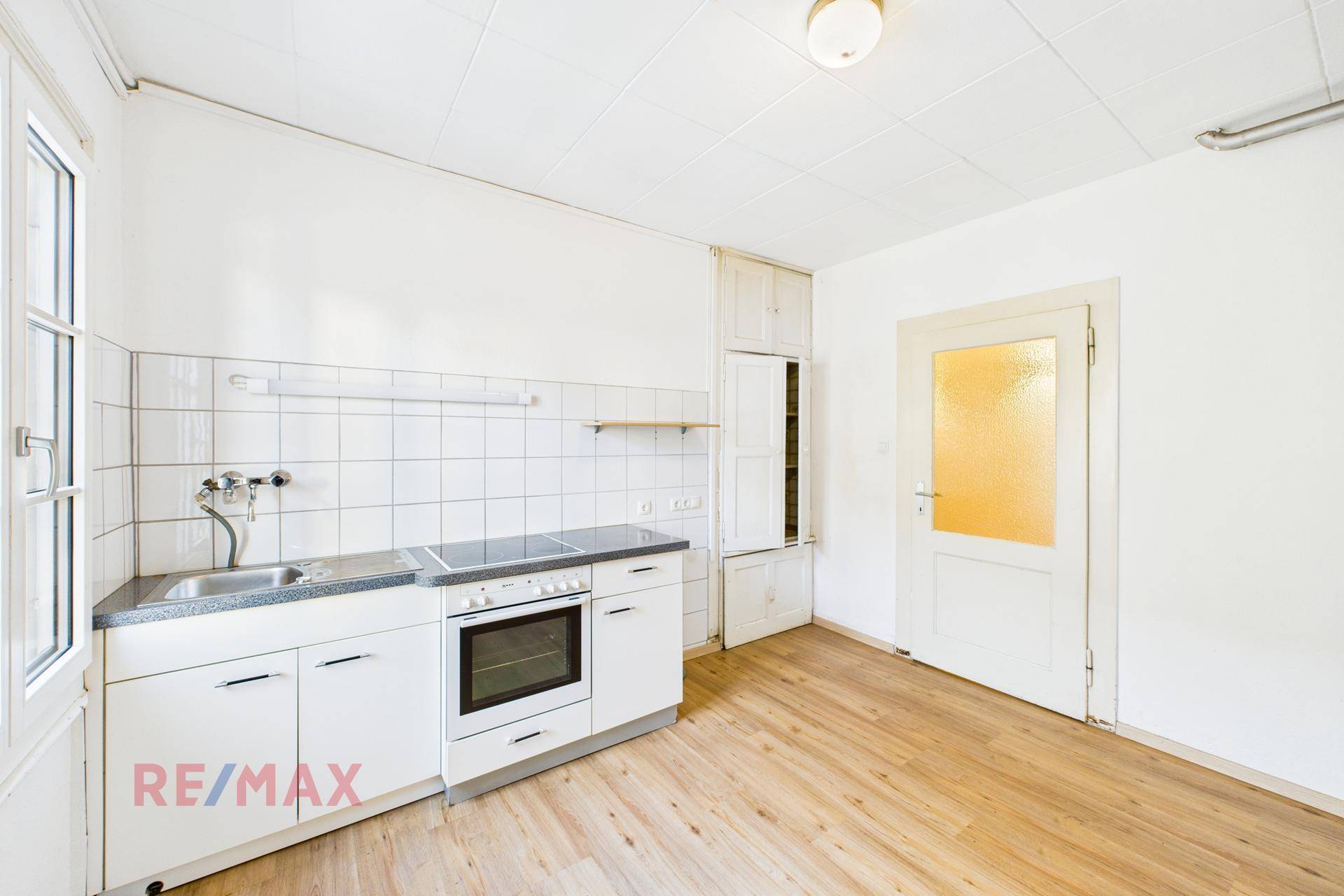 Funktionale Küche mit weißen Unterschränken, Herd und Fenster, ideal für eine Renovierung.