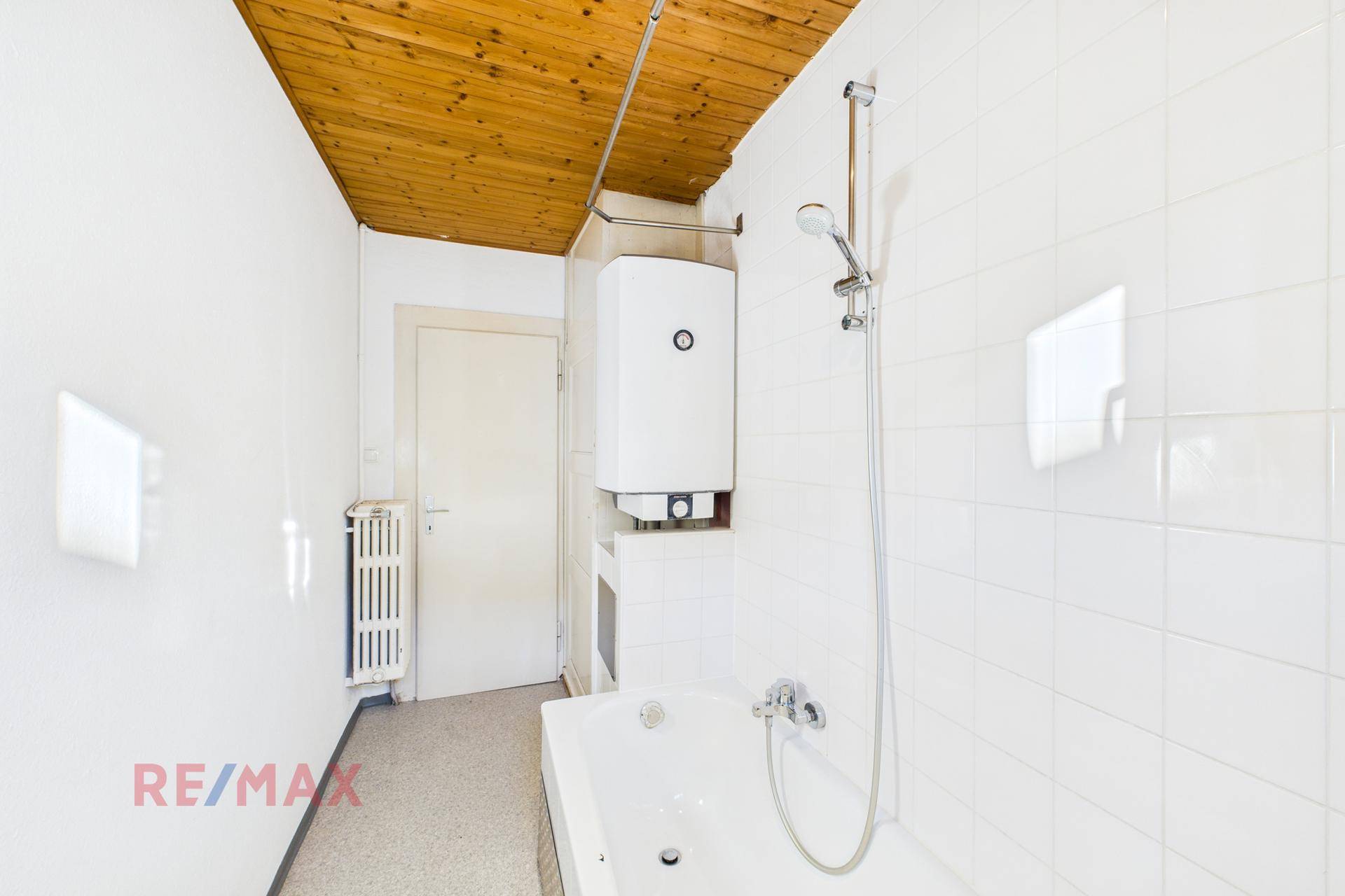 Helles Badezimmer mit Badewanne, Warmwasserboiler und Holzdecke, funktional eingerichtet.