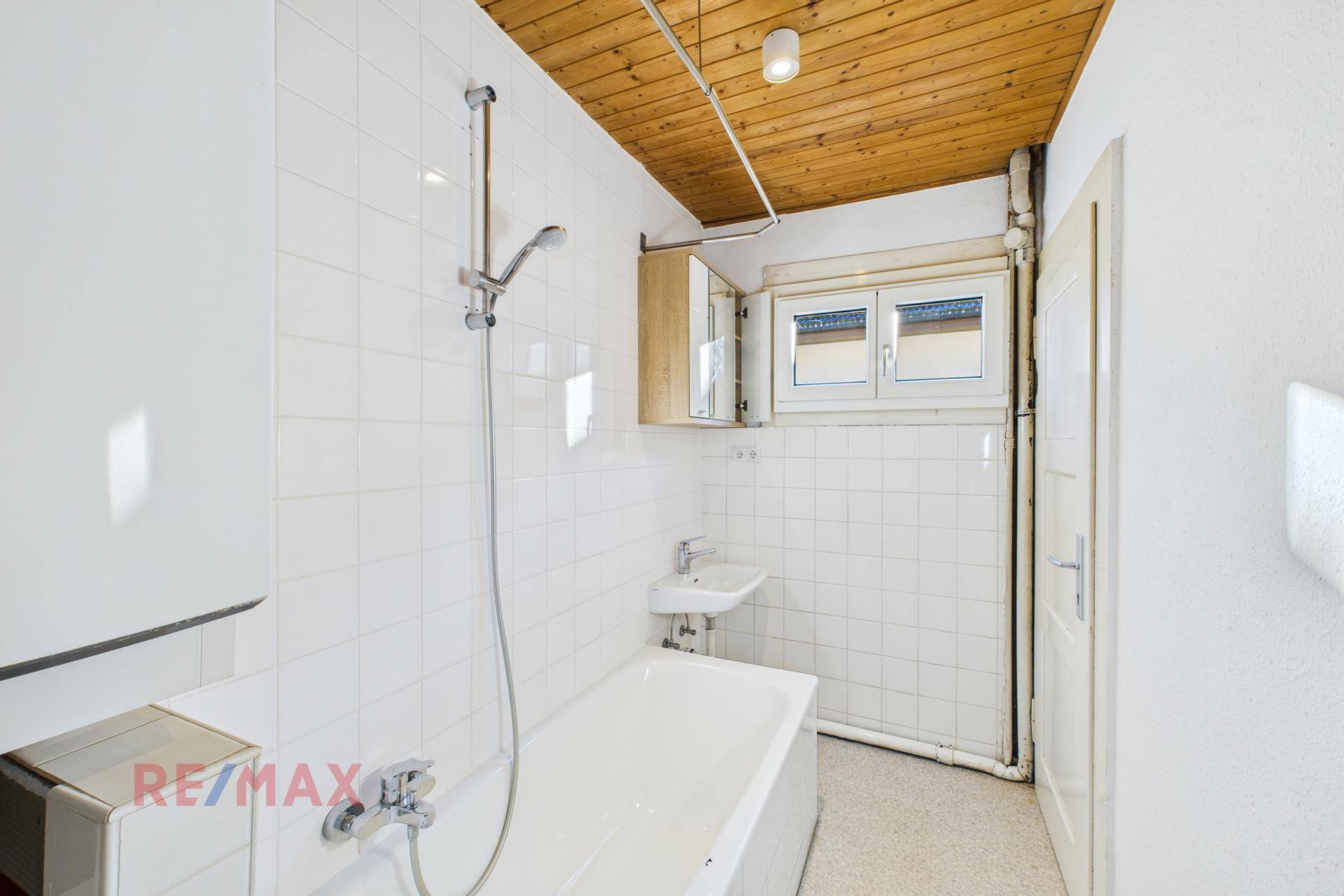 Badezimmer mit Badewanne, Dusche und Holzdecke, mit Fenster für Tageslicht.