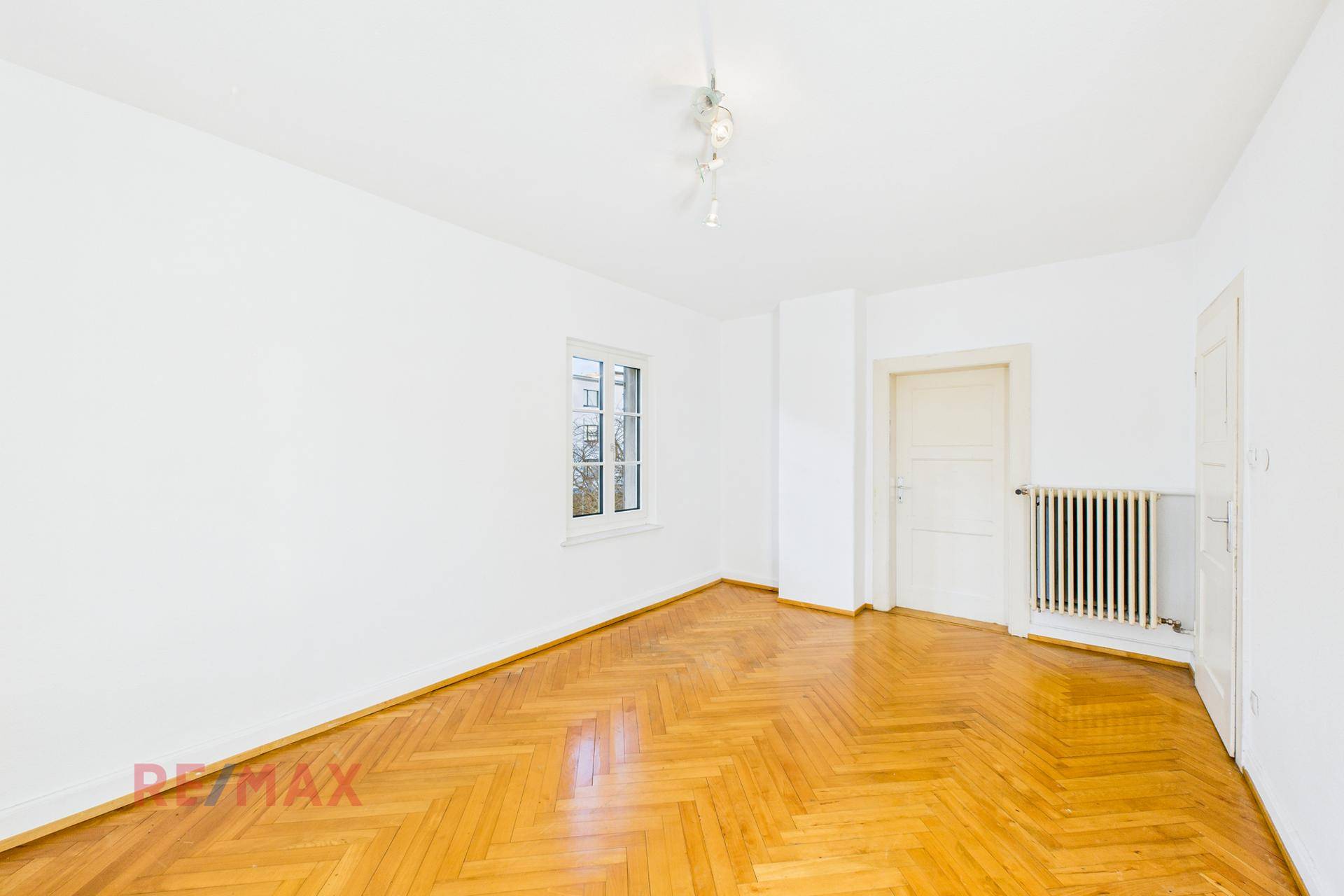 Helles Wohnzimmer mit Fischgrätparkett und großem Fenster, bereit zur Einrichtung.