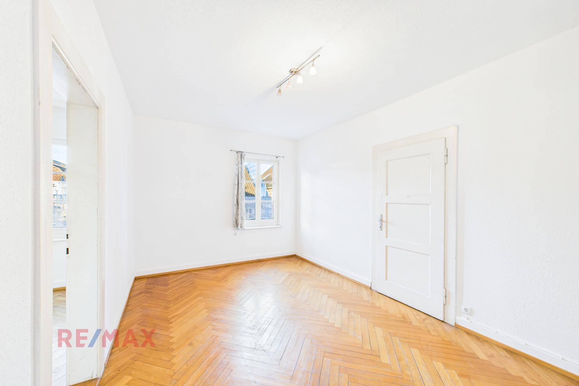 Helles Wohnzimmer mit Fischgrätparkett und Fenster, ideal für gemütliche Stunden.