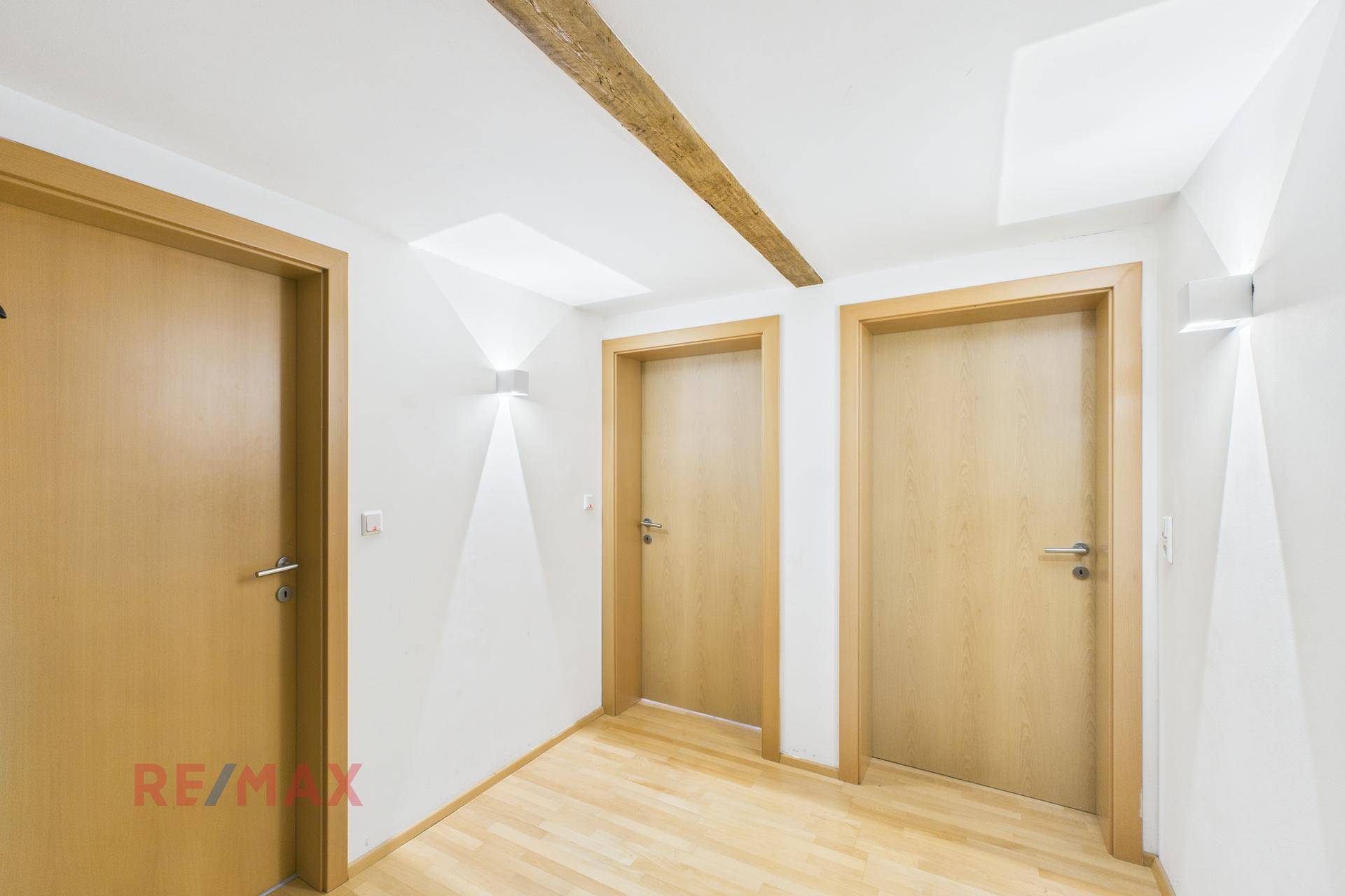 Heller Flur mit Holzbalken und mehreren Türen, modern beleuchtet.