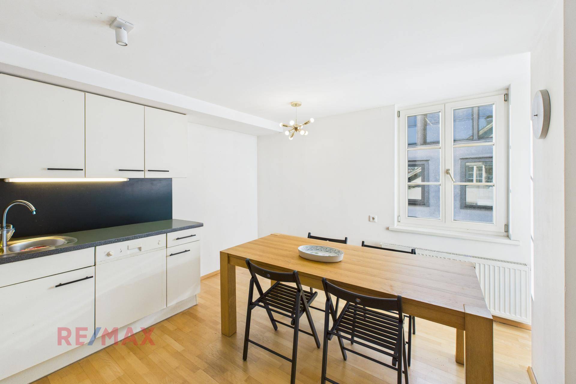 Moderne Einbauküche mit Essbereich, weißen Schränken und Holztisch.
