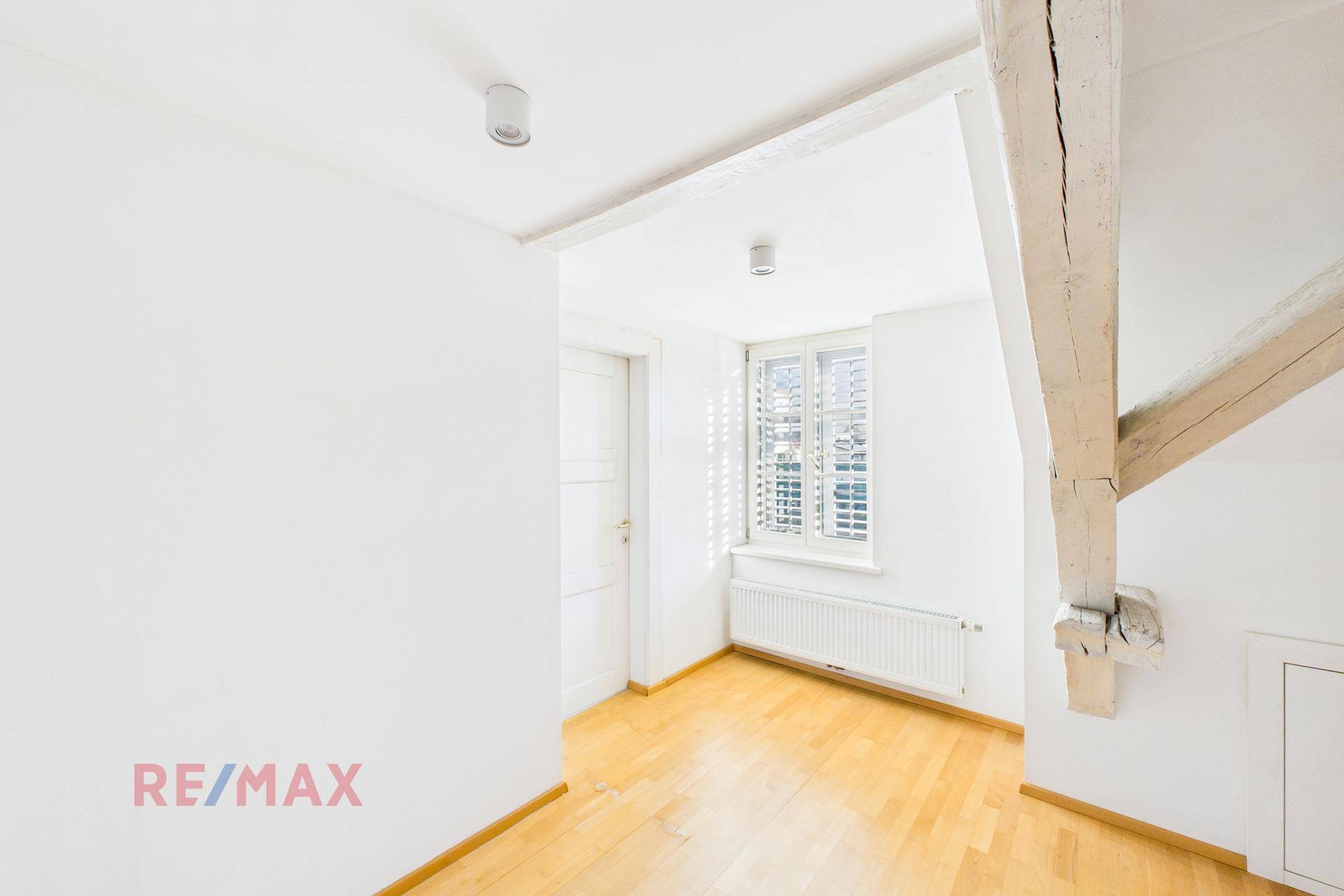 Helles Schlafzimmer im Dachgeschoss mit Holzbalken und Fenster, gemütlich und einladend.