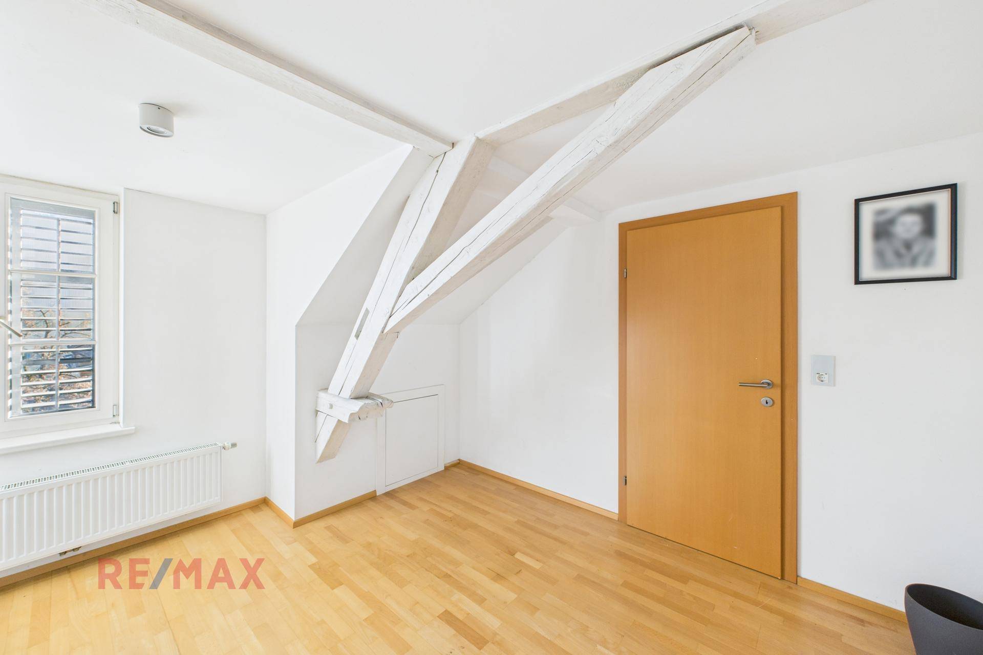 Schlafzimmer im Dachgeschoss mit sichtbaren Holzbalken und Fenster, mit Holzboden.