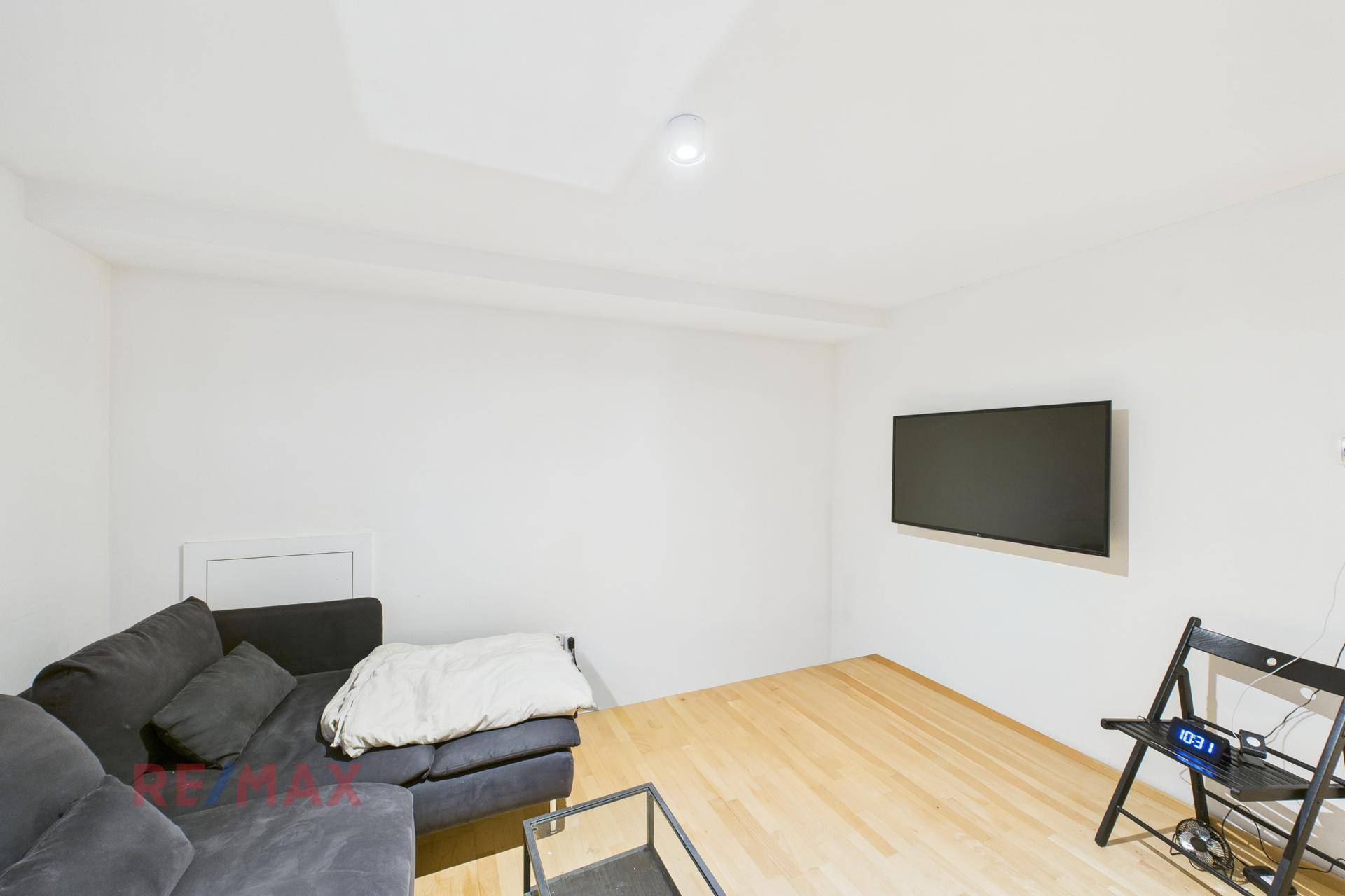 Modernes Wohnzimmer mit Wandfernseher, Sofa und Holzboden, hell und funktional.