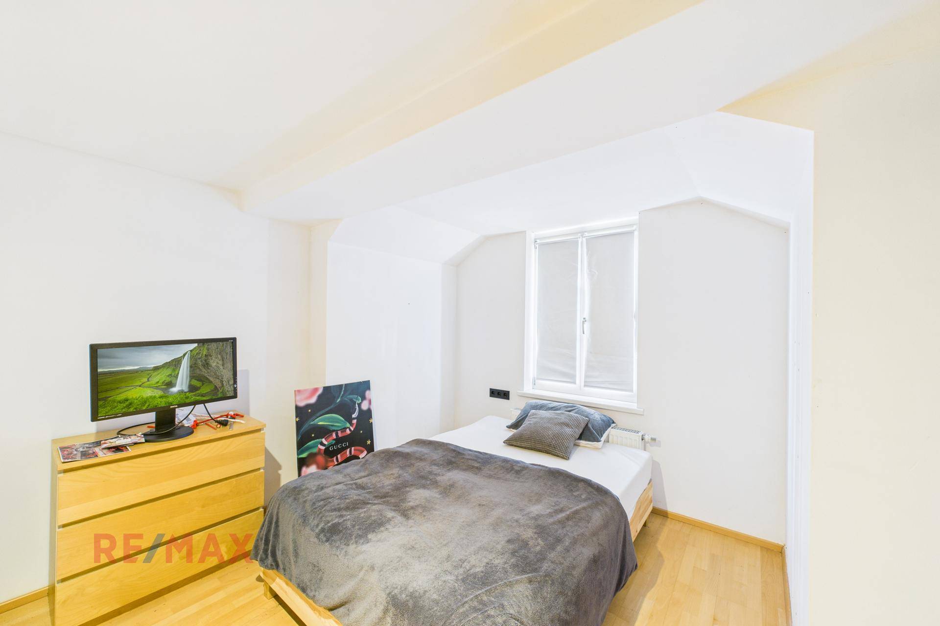 Schlafzimmer mit Bett, Kommode und Fernseher, mit Fenster und Holzboden.
