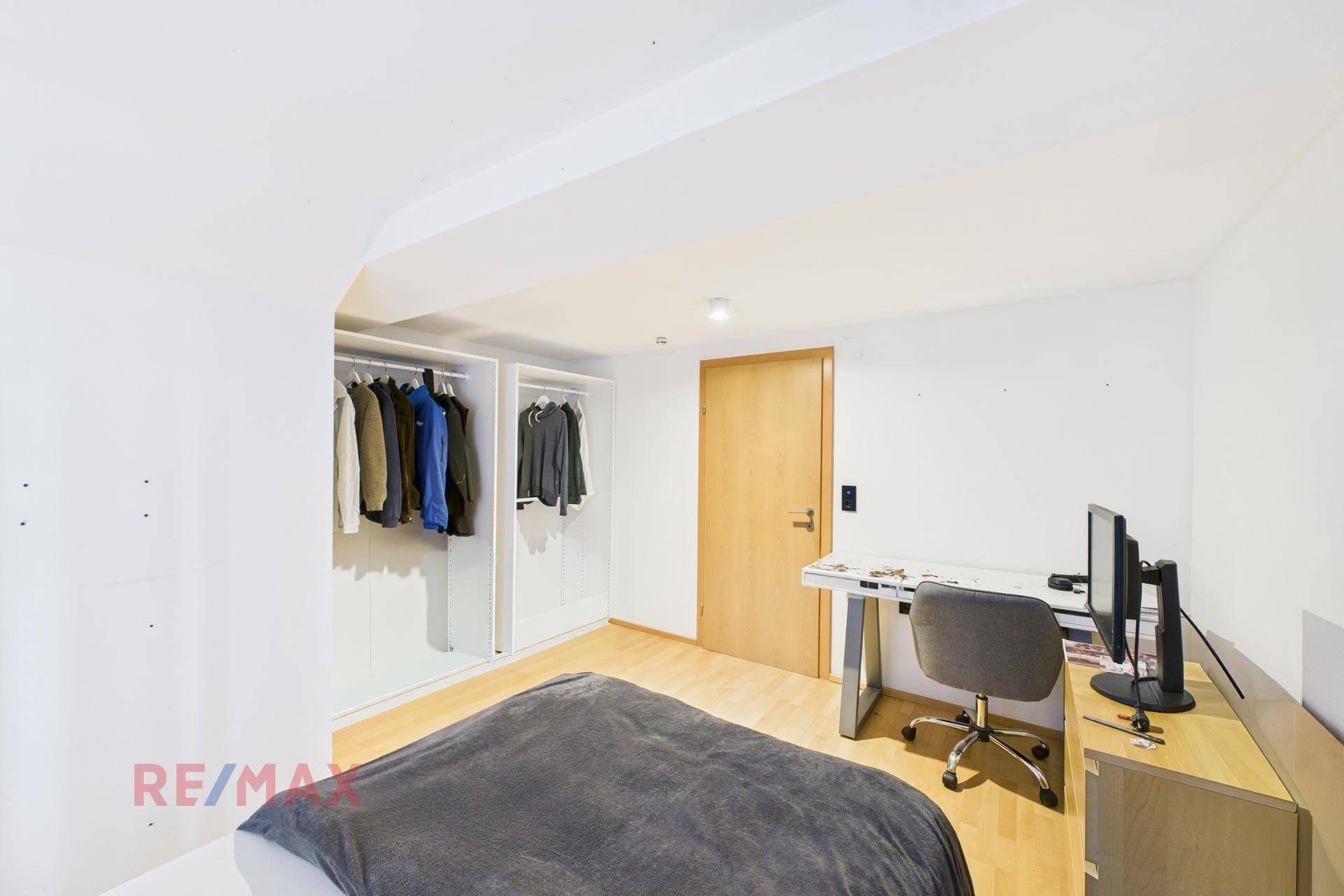 Schlafzimmer mit Bett, Schreibtisch und offenem Kleiderschrank, mit Holzboden.