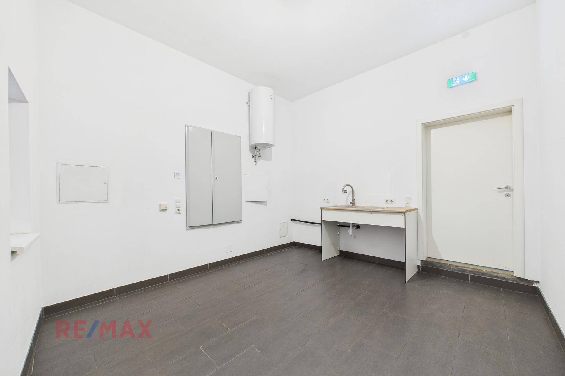 Funktionaler Raum mit Spülbecken, Warmwasserbereiter und dunklem Fliesenboden.