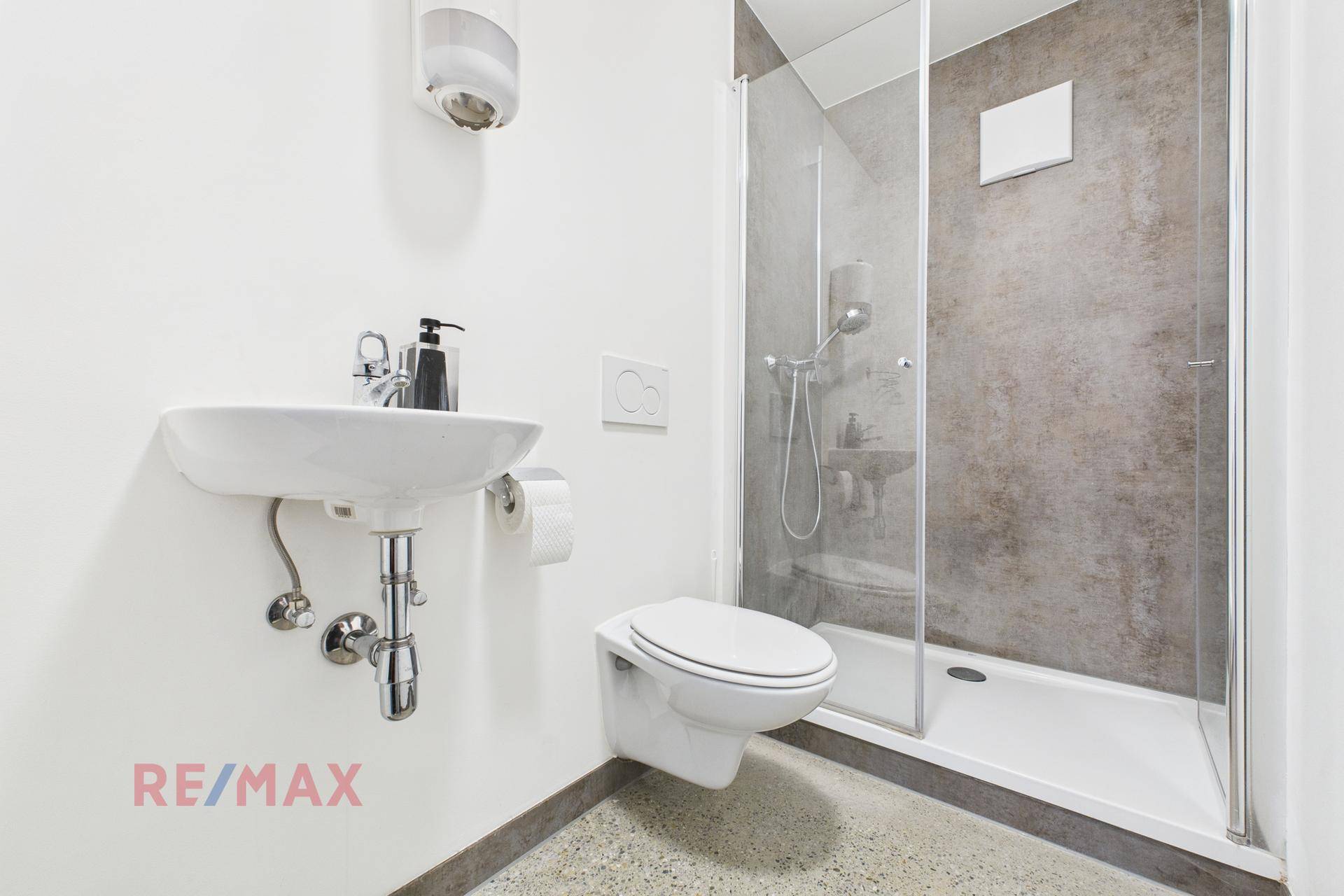 Modernes Badezimmer mit Duschkabine, wandhängendem WC und kleinem Waschbecken.