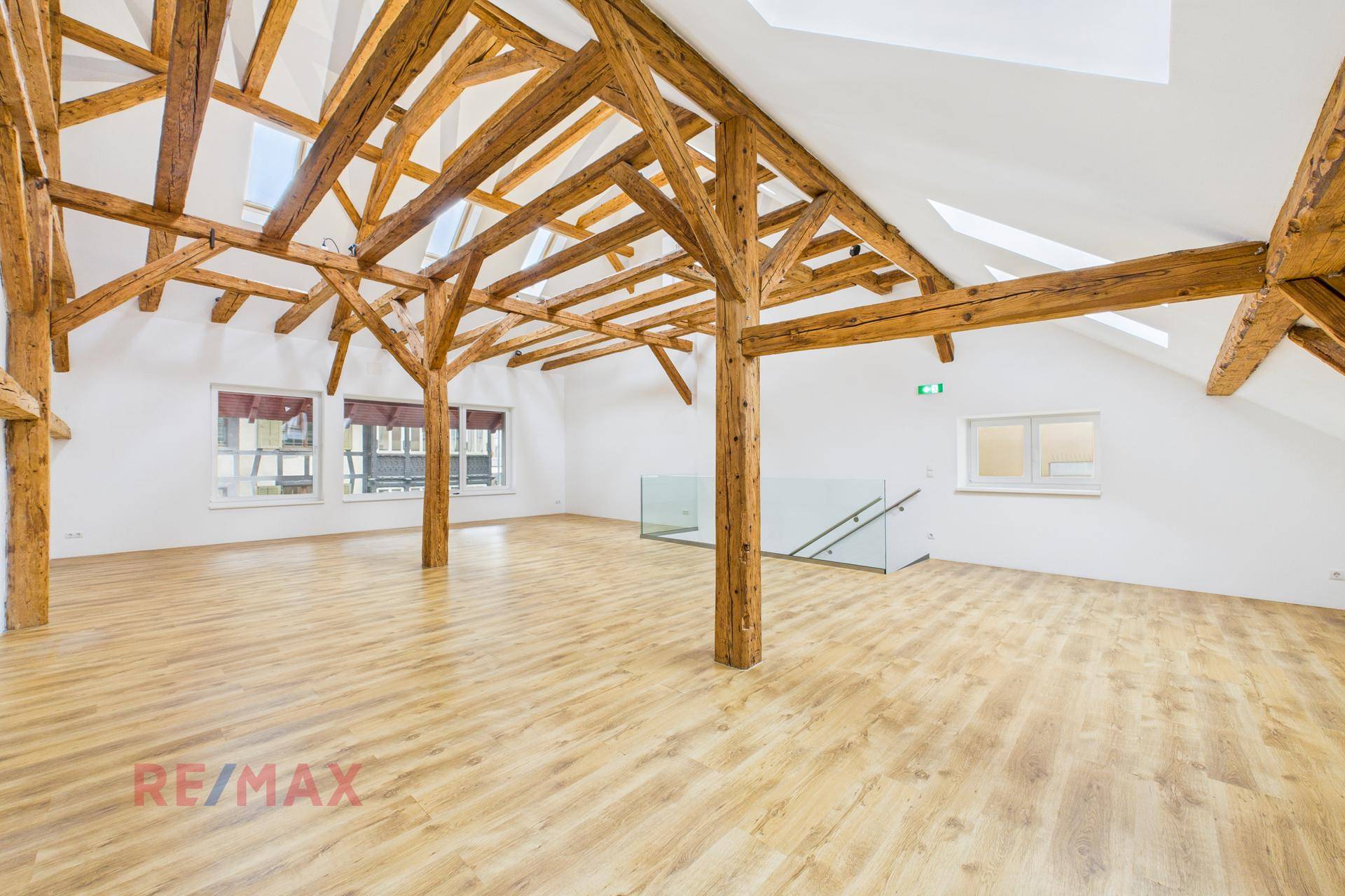 Heller Dachgeschossraum mit sichtbaren Holzbalken, Laminatboden und Fenstern.