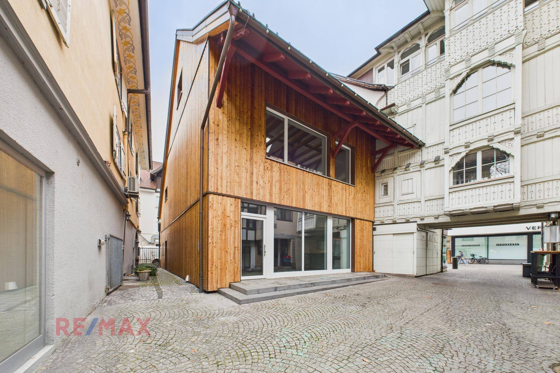 Attraktives Gebäude mit Holzfassade und großen Fenstern an einem gepflasterten Innenhof.
