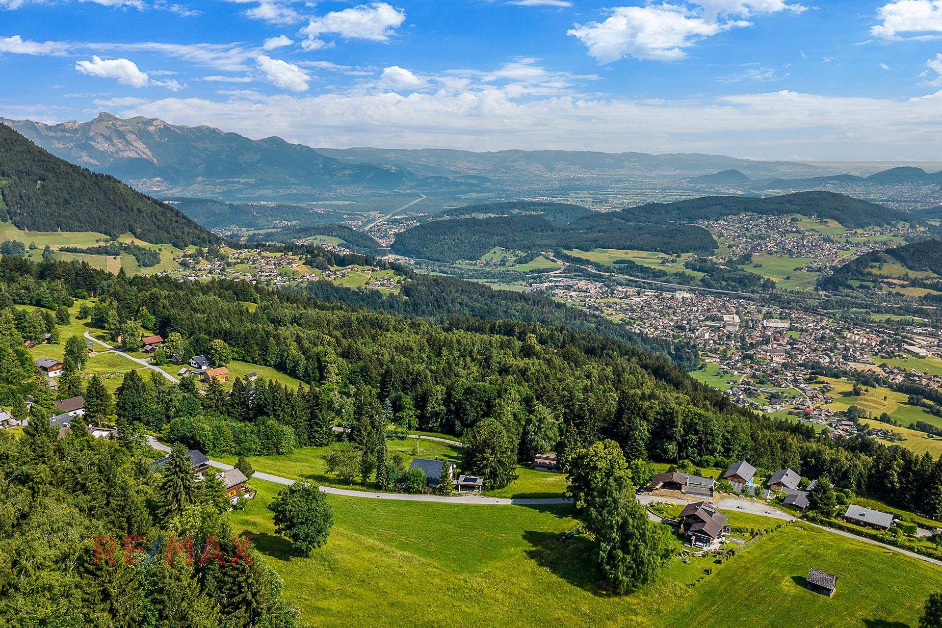 Panoramische Luftaufnahme eines malerischen Dorfes eingebettet in eine grüne Berglandschaft.