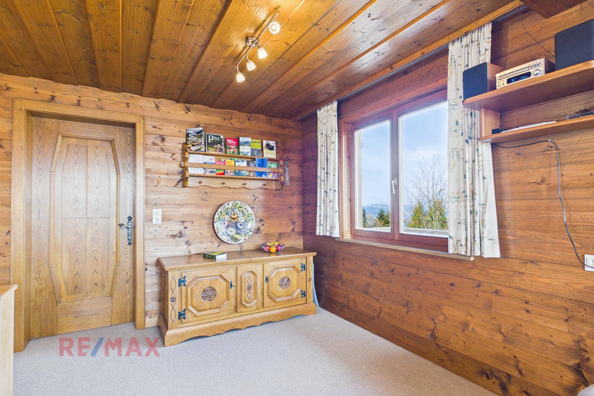 Wohnraum mit Holztäfelung, Teppichboden und traditionellem Holzschrank.