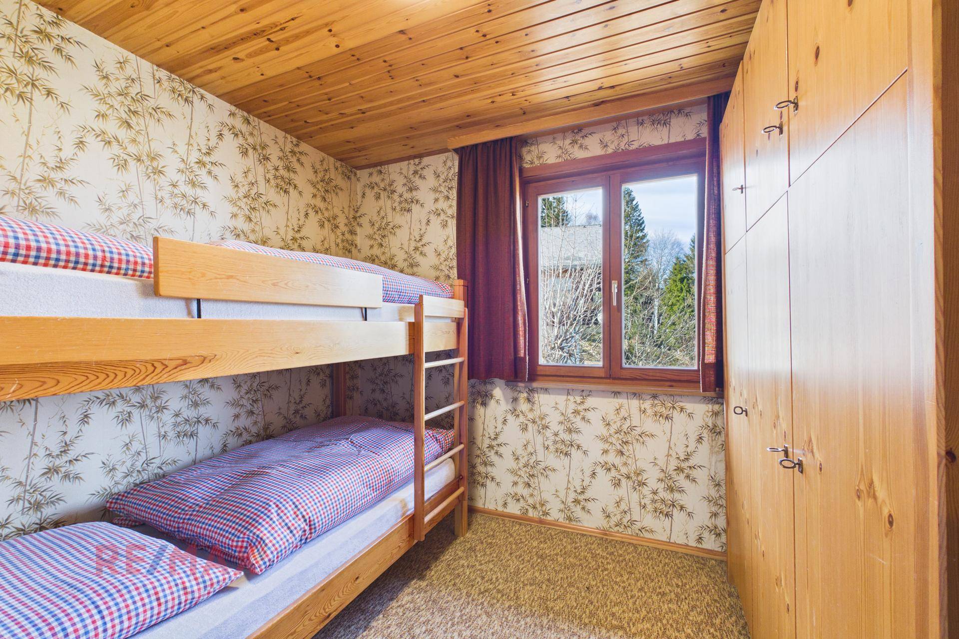 Kinderzimmer mit Etagenbett, Holzschrank und gemusterter Tapete.