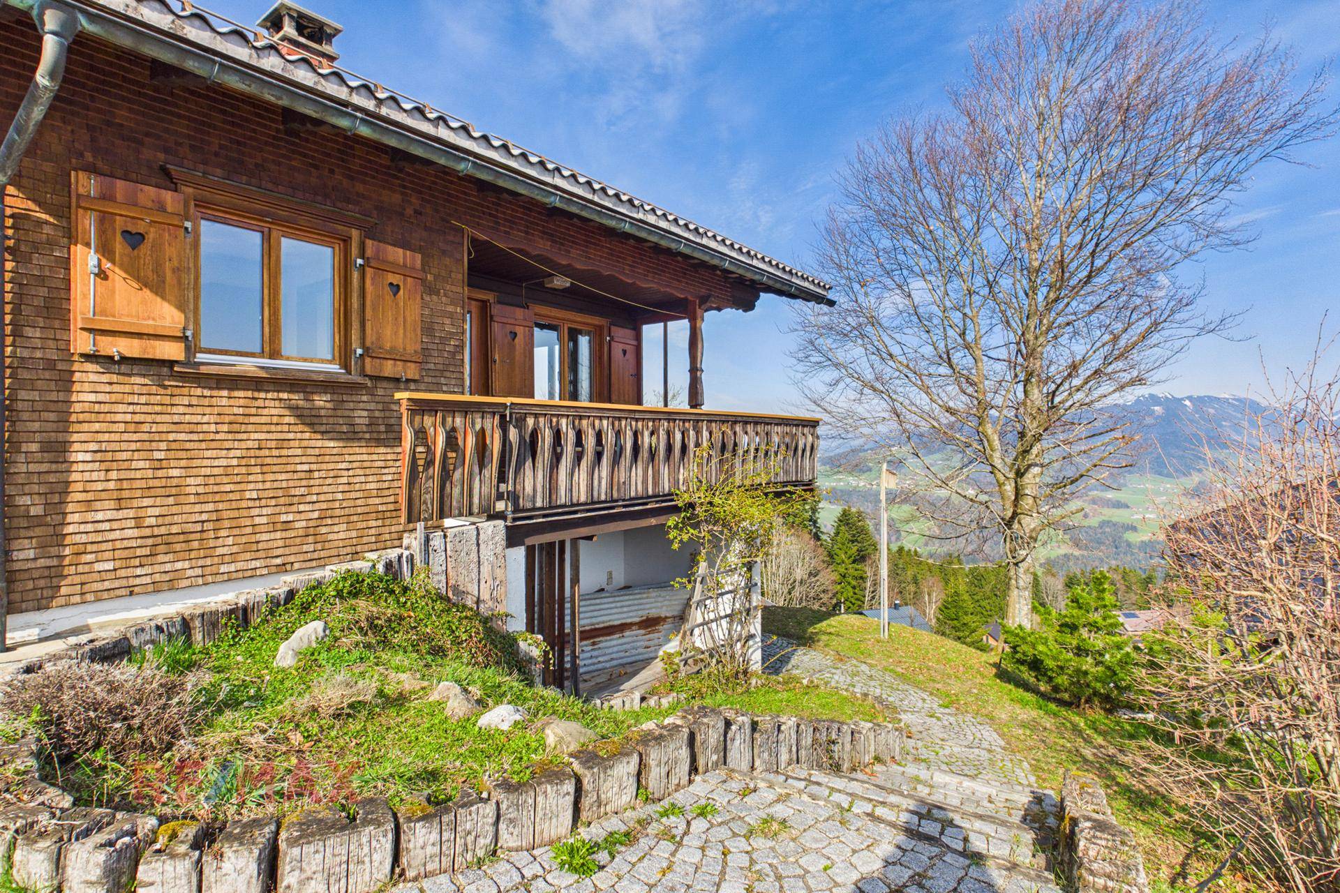 Charmantes Holzhaus mit Balkon und malerischem Bergblick unter blauem Himmel.