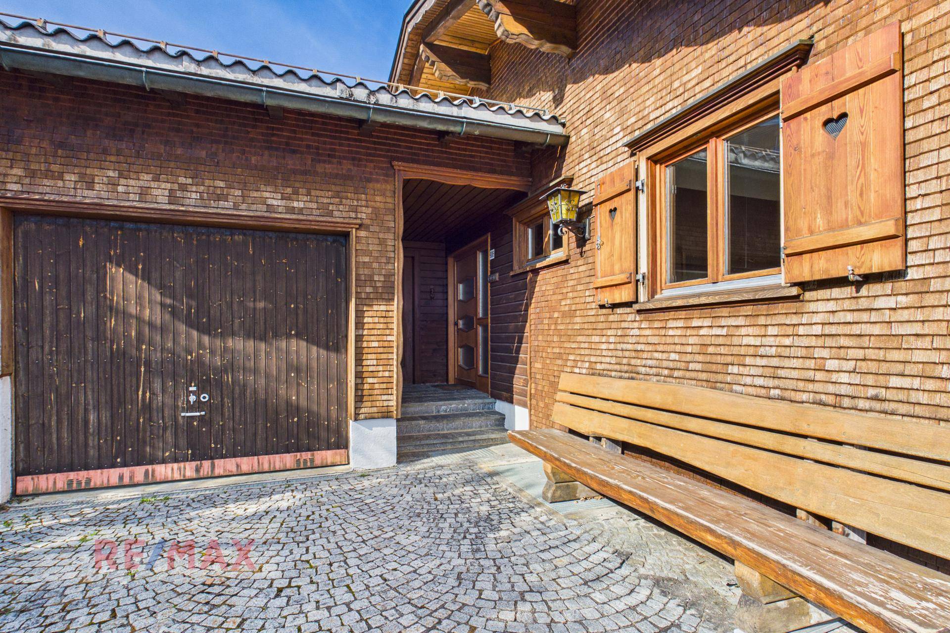 Eingangsbereich des Holzhauses mit Garage und traditioneller Holzbank.