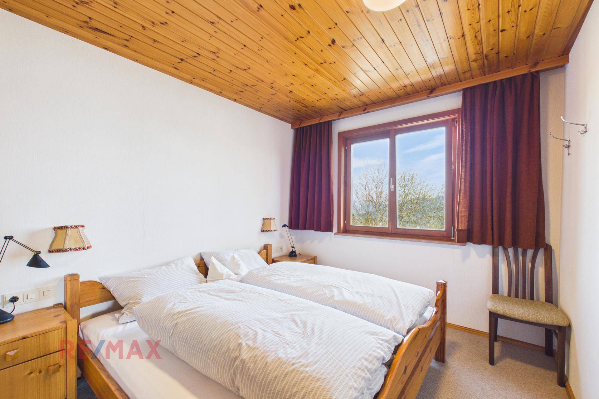 Helles Schlafzimmer mit zwei Einzelbetten, Holzdecke und Teppichboden.