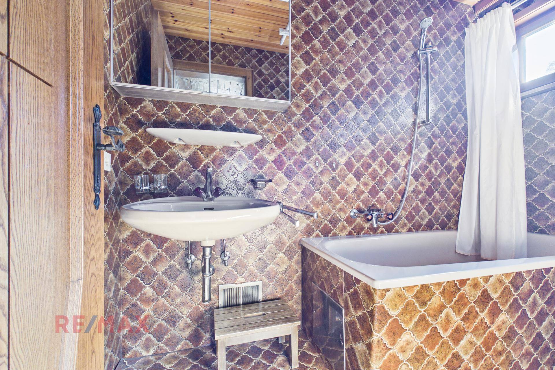 Badezimmer im 80er-Jahre-Stil mit Badewanne, Waschbecken und gemusterten Fliesen.