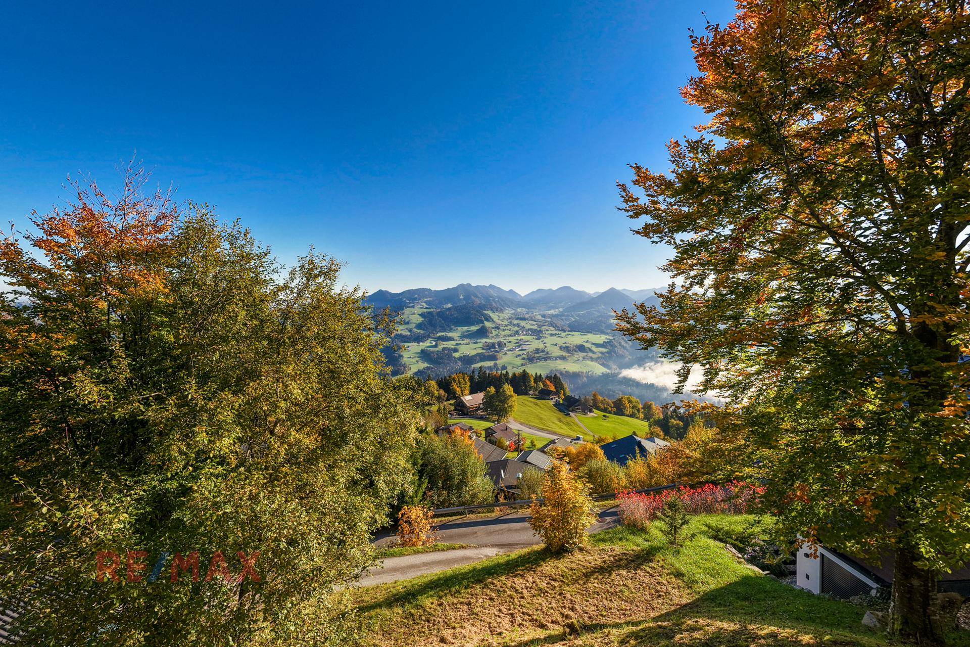 Malerische Herbstlandschaft mit Häusern und Bergen im Hintergrund.