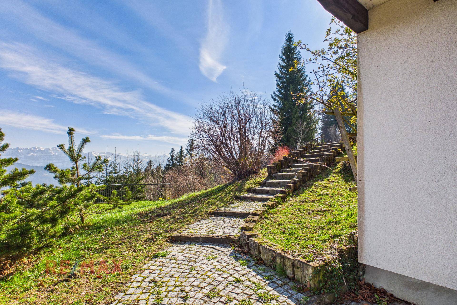 Steiler gepflasterter Weg führt durch grüne Landschaft mit Bergblick.