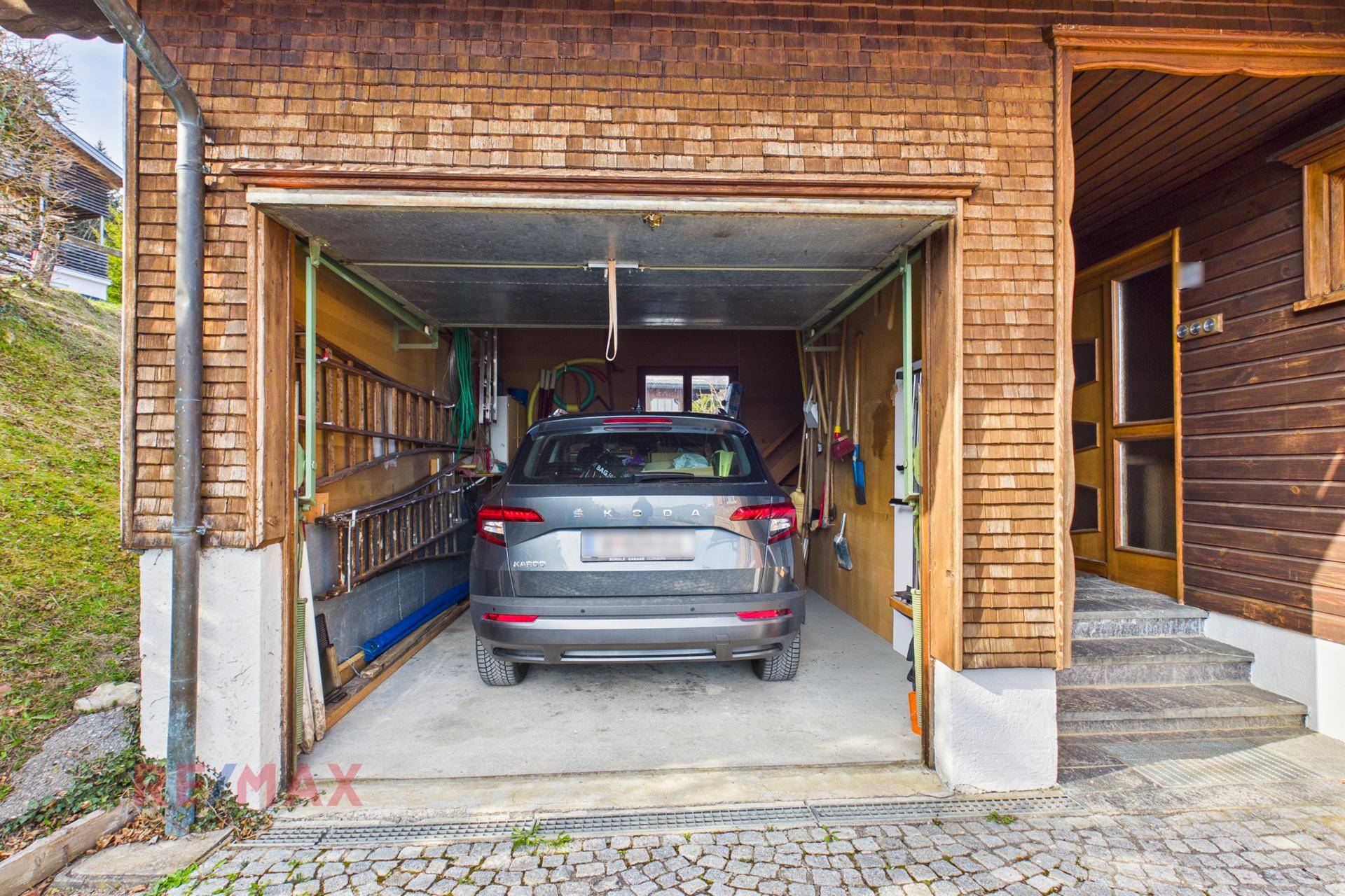 Offene Garage mit geparktem Auto und Stauraum für Werkzeuge.