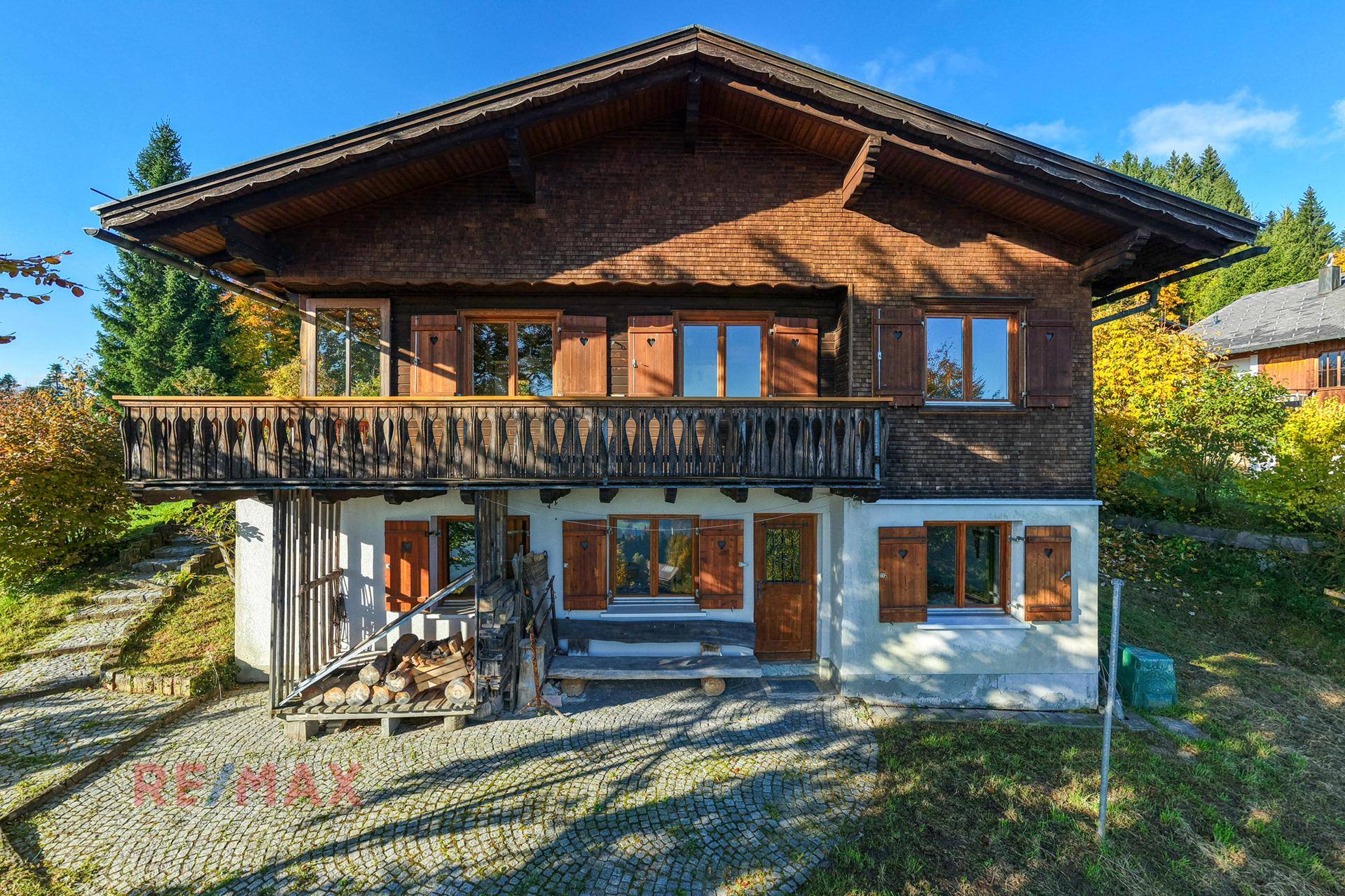 Traditionelles Holzhaus mit Balkon und gepflasterter Auffahrt in sonniger Lage.