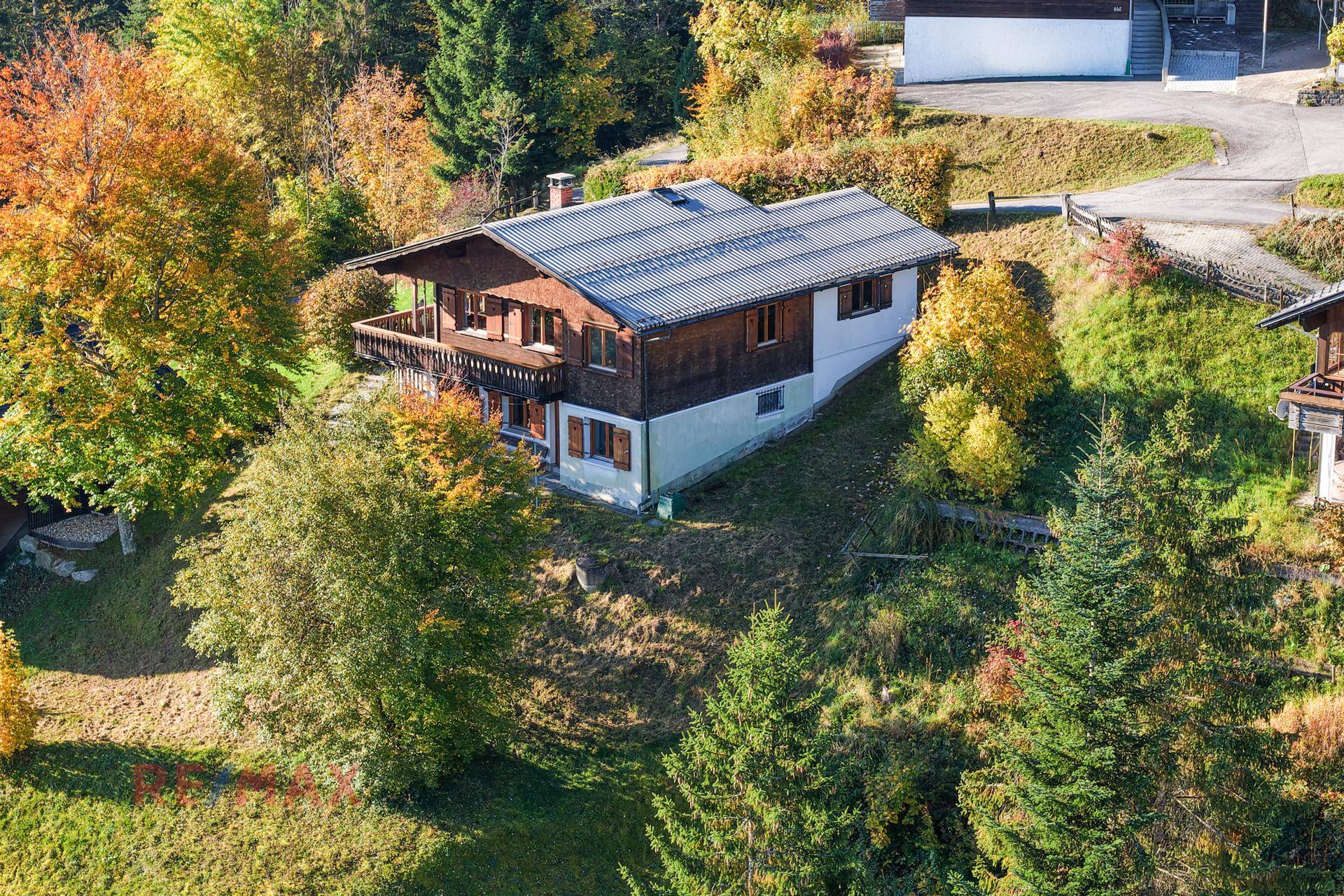 Luftaufnahme des Holzhauses eingebettet in die grüne Hügellandschaft mit Herbstbäumen.
