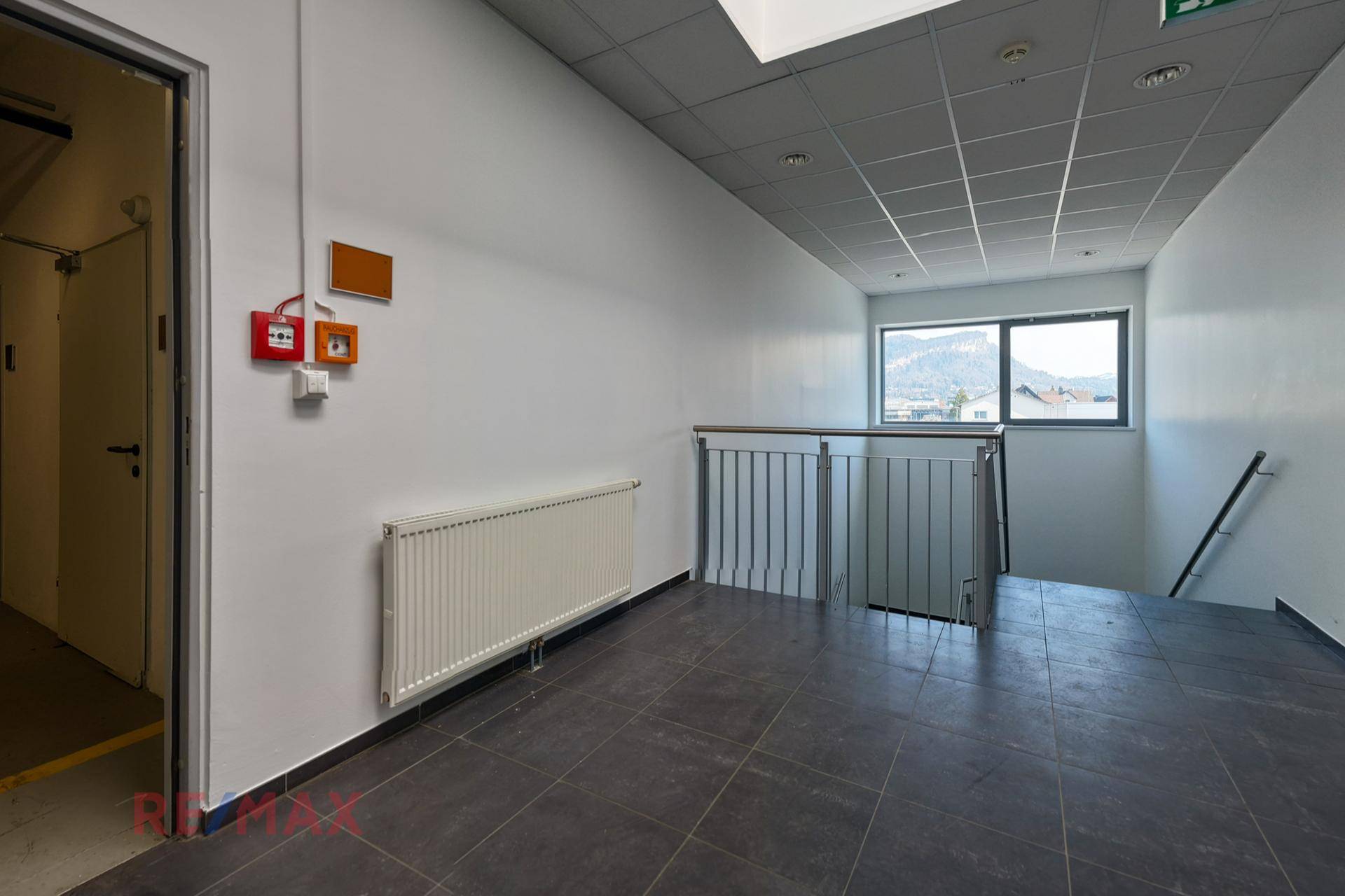 Flur oder Treppenabsatz mit dunklem Fliesenboden, Heizkörper und einem Fenster mit Blick auf die umliegende Landschaft.