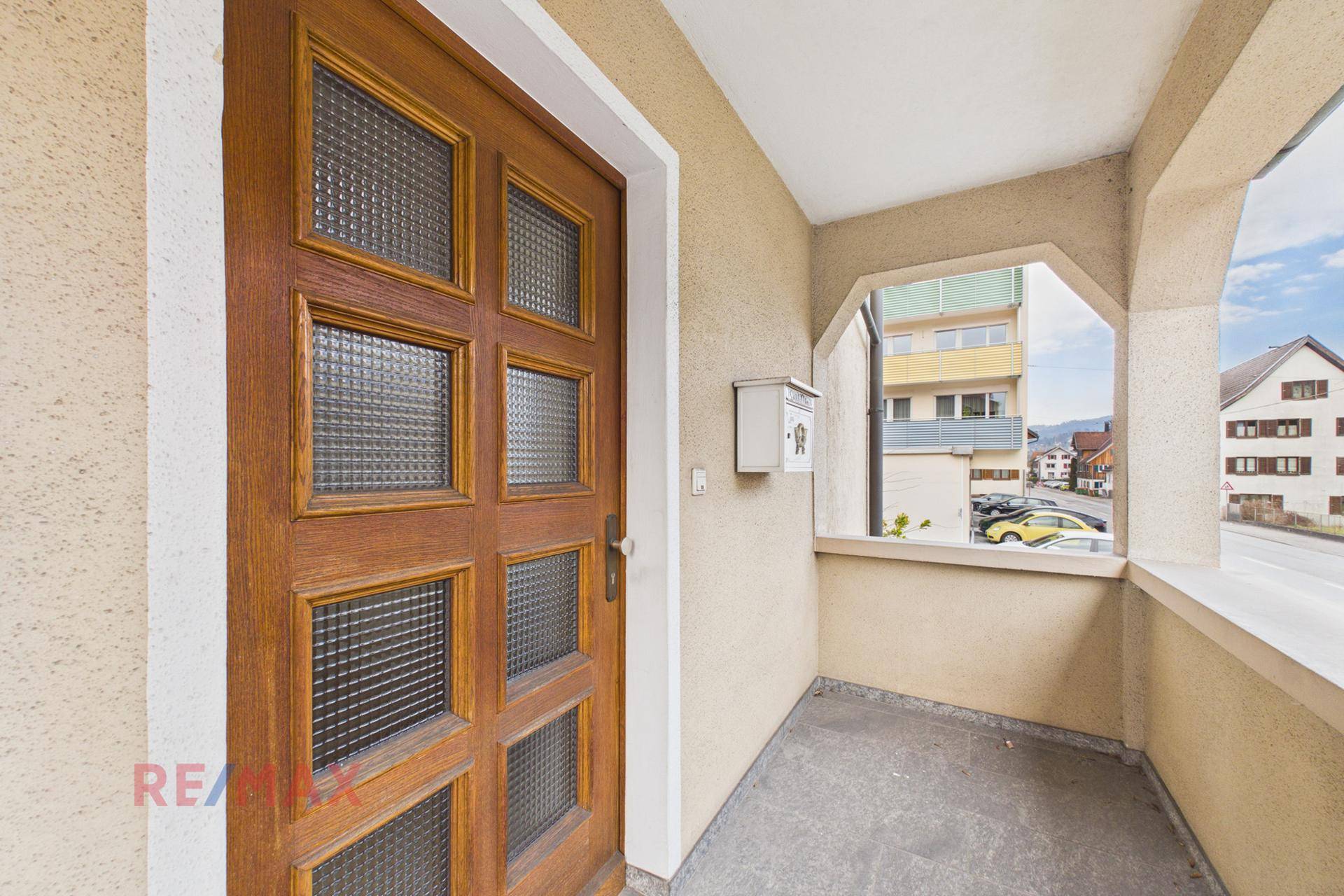 Überdachter Eingangsbereich mit Holztür und Blick auf die Straße und umliegende Gebäude.