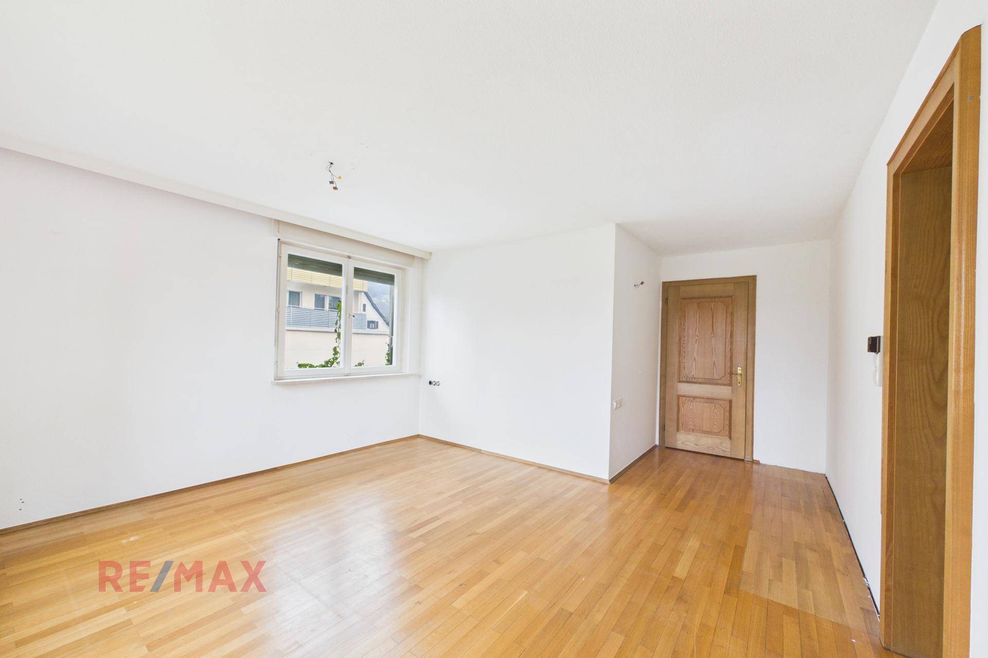 Leeres Zimmer mit Parkettboden und Fenster, ideal als Schlaf- oder Arbeitszimmer.