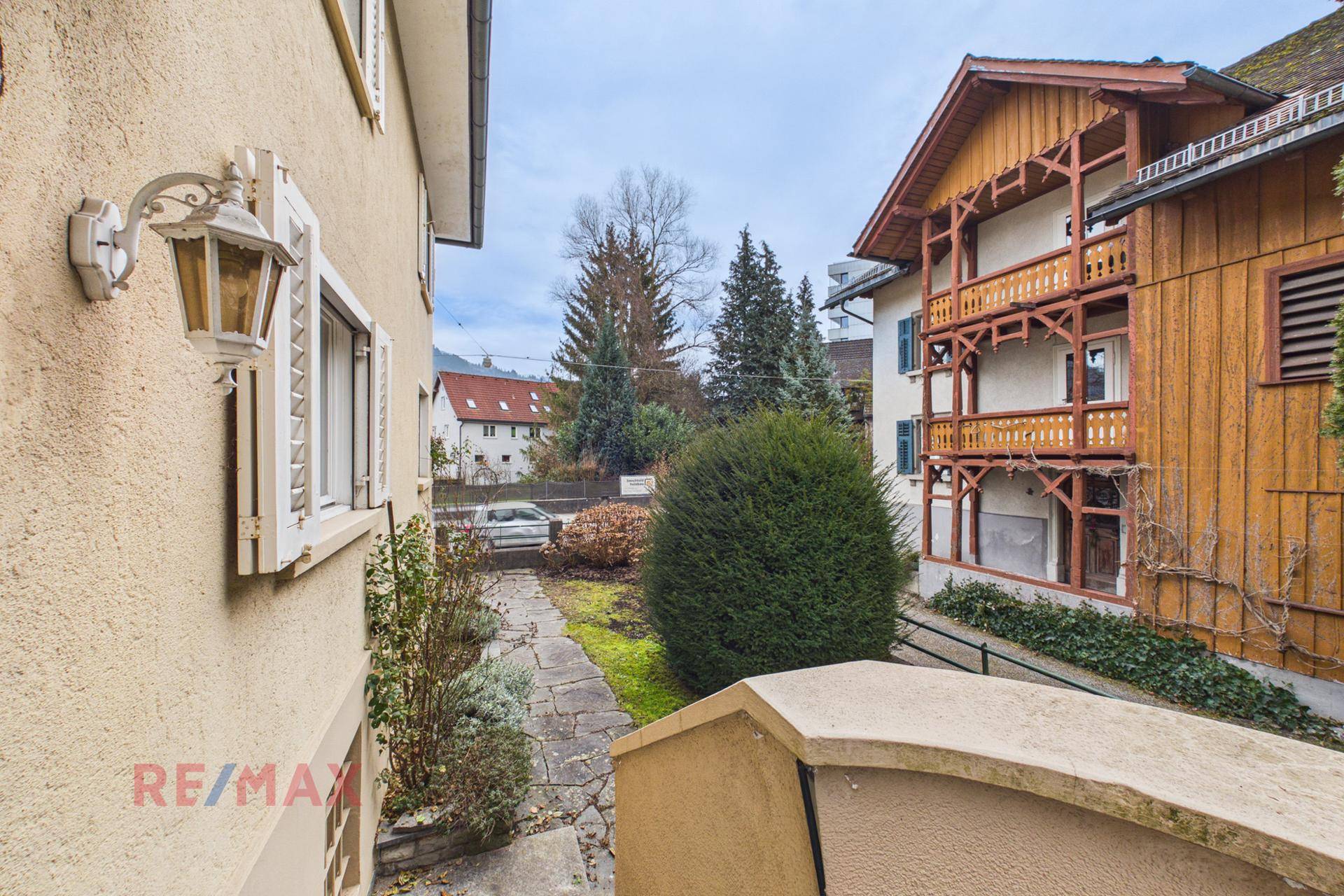 Seitenansicht des Hauses mit Gartenweg, Sträuchern und angrenzendem Holzhaus.
