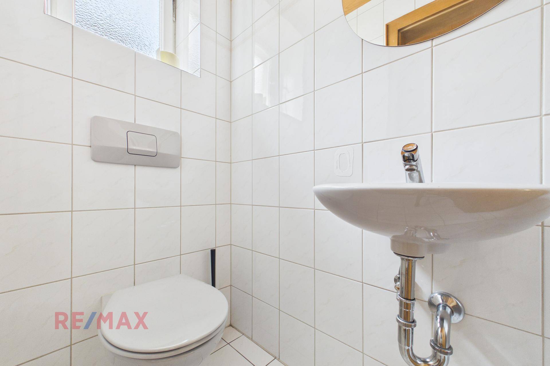Kleines WC mit weißen Fliesen und wandmontierter Toilette.