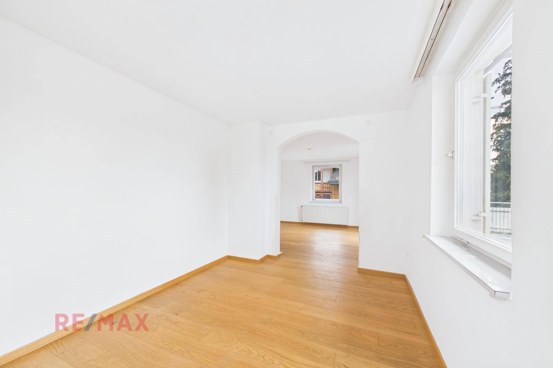 Geräumiger Wohnbereich mit Parkettboden und natürlichem Lichteinfall durch die Fenster.