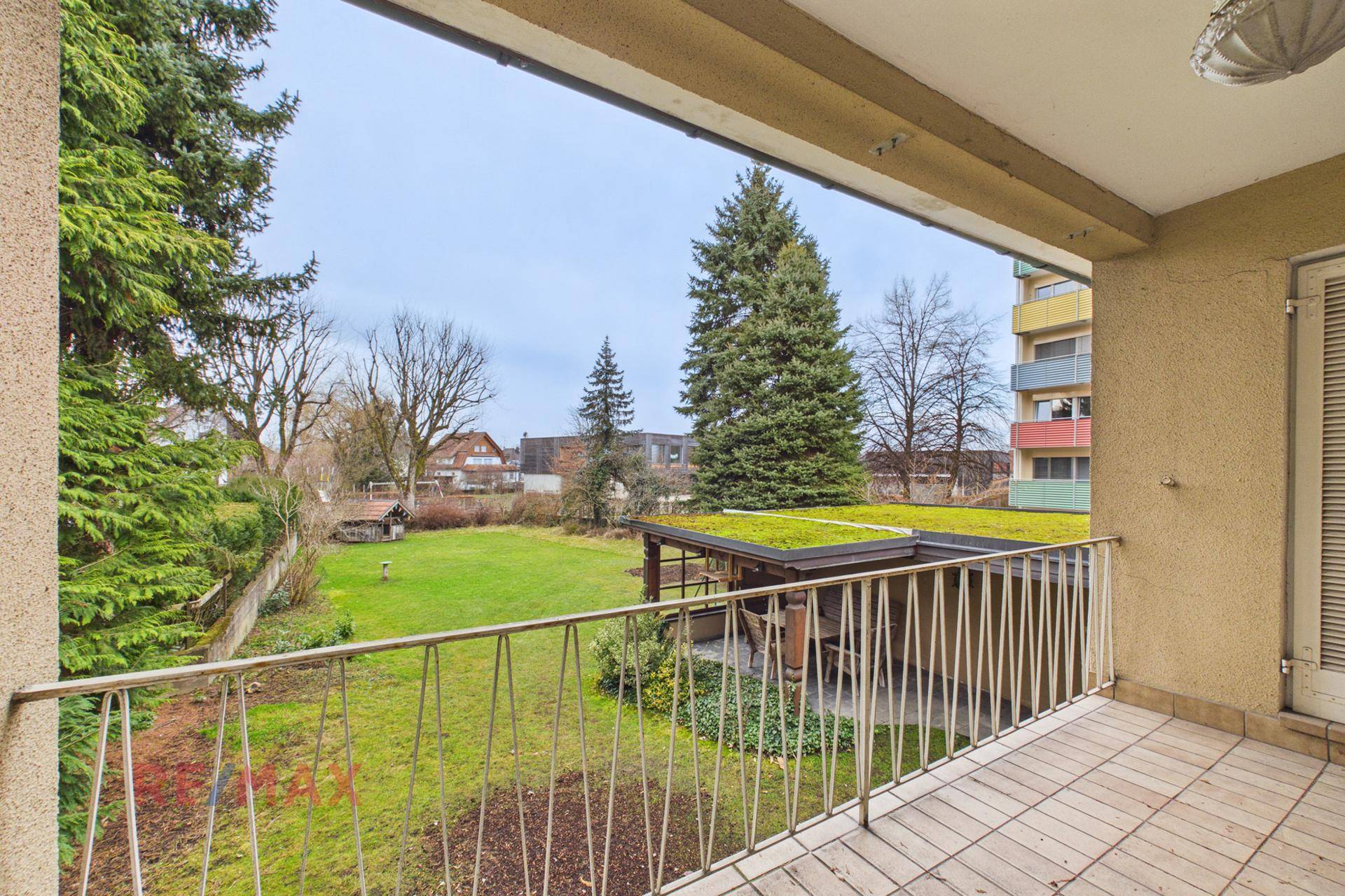 Balkon mit Blick auf den grünen Garten und die umliegenden Gebäude.