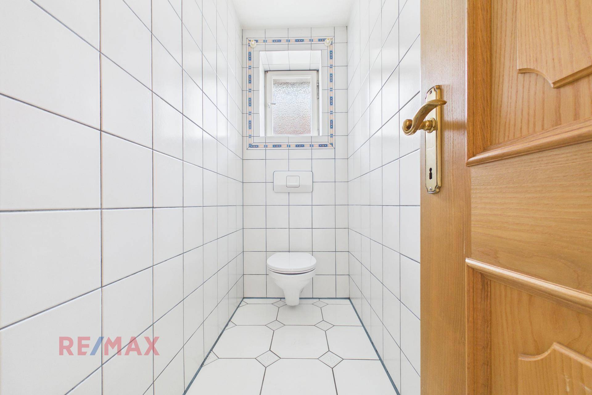 Kleines WC mit weißen Fliesen, wandmontierter Toilette und Fenster.