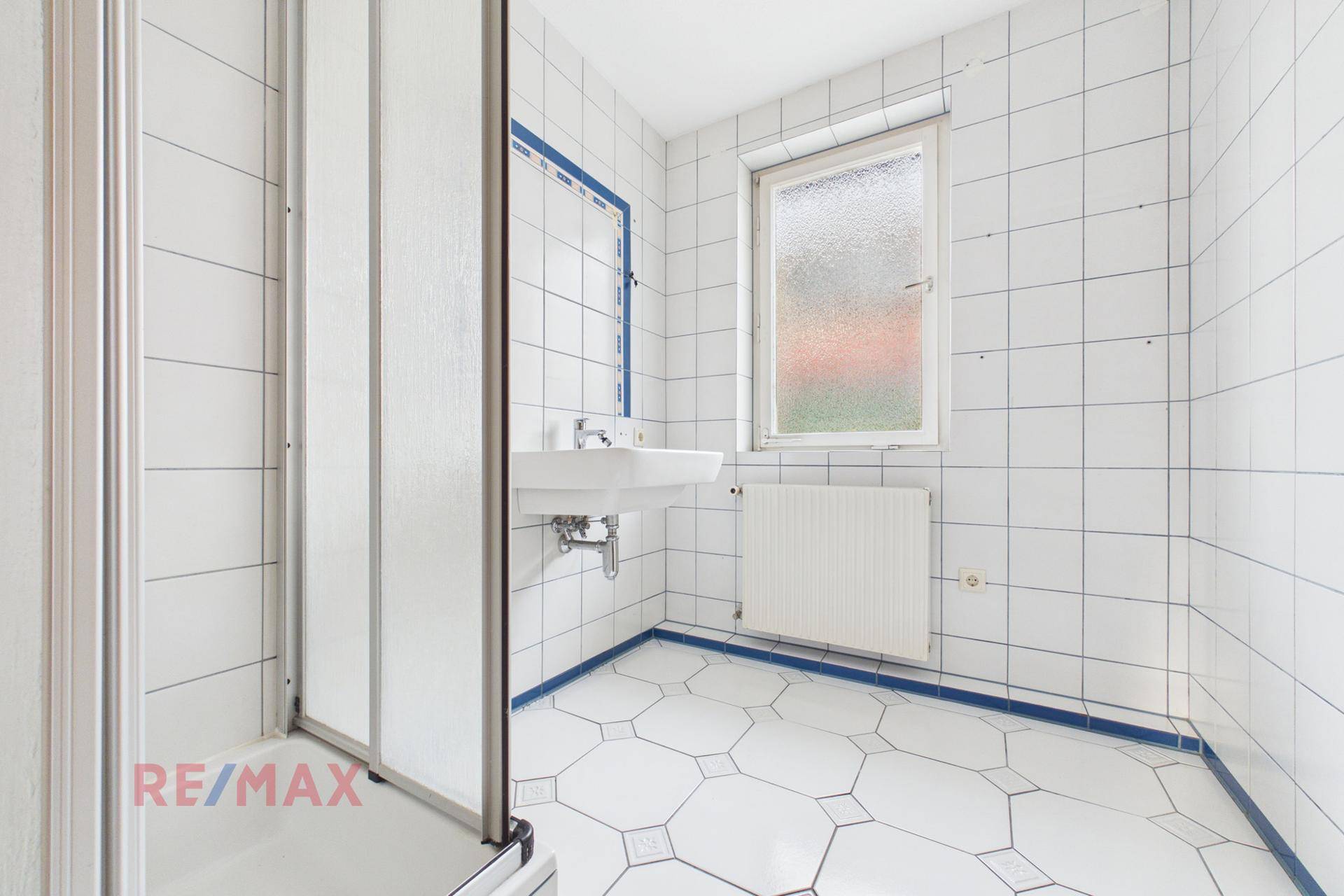 Badezimmer mit weißen Fliesen, Duschkabine und Fenster, in gutem Zustand.