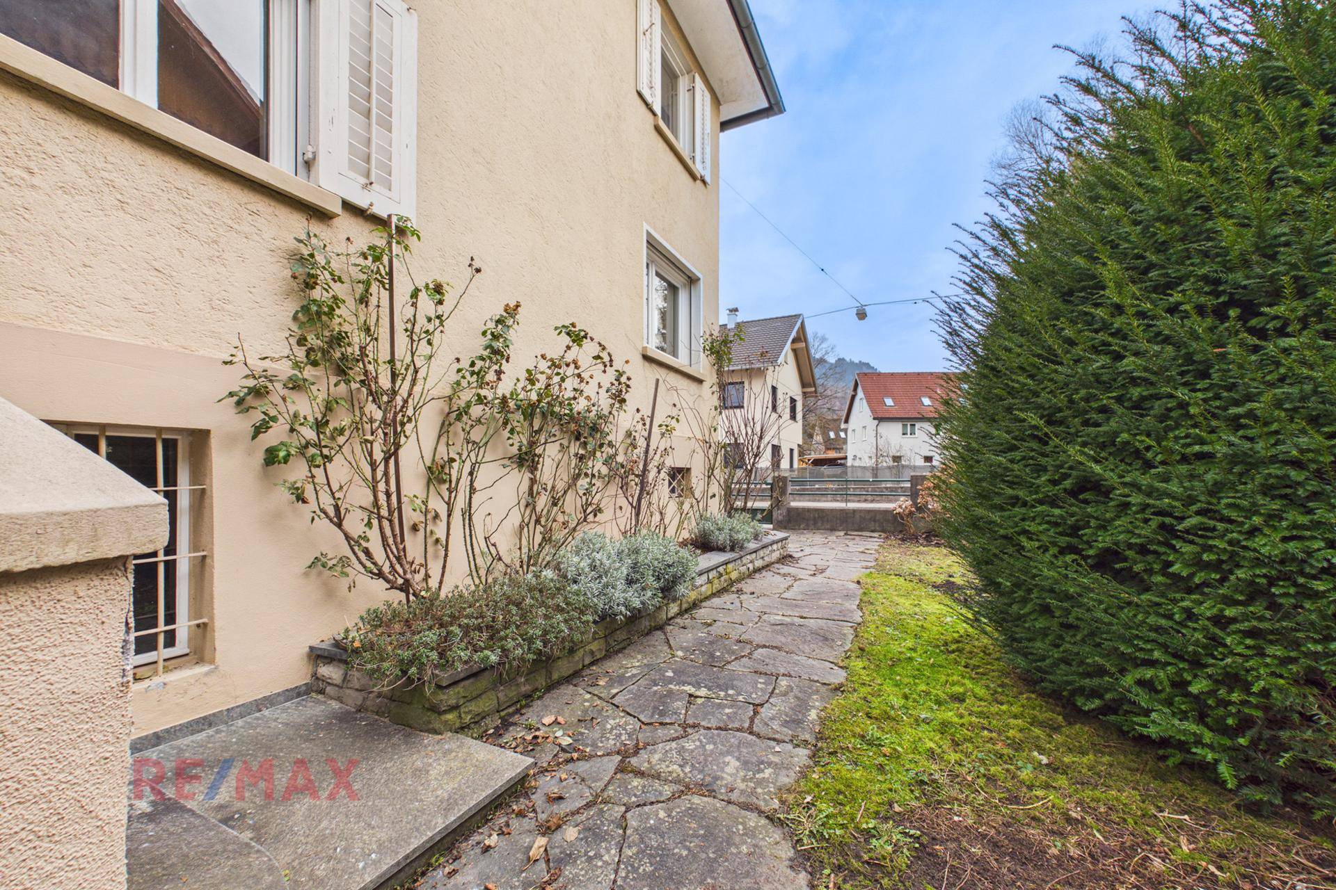 Seitlicher Gartenweg mit Steinplatten und bepflanzten Beeten entlang der Hauswand.