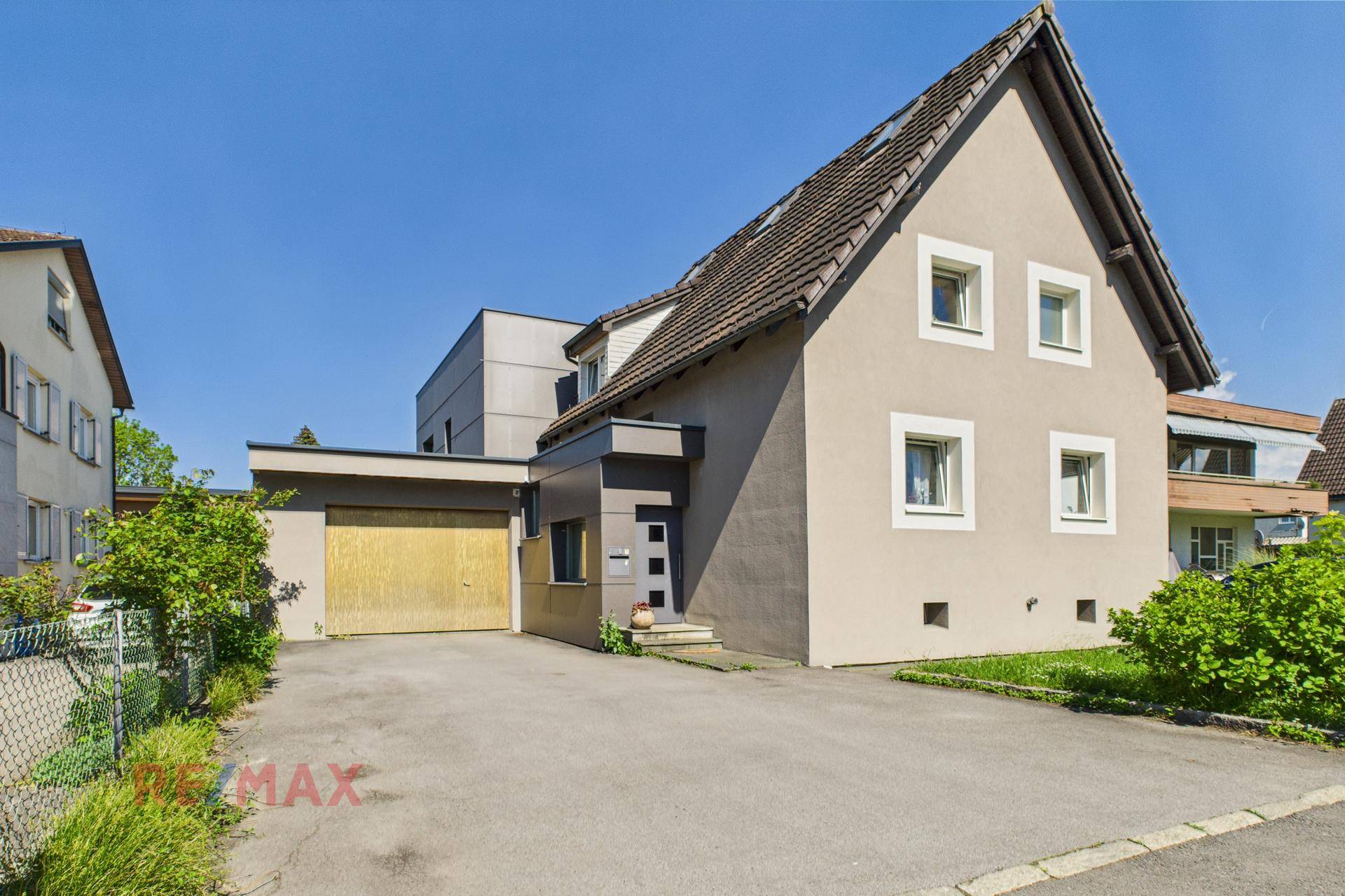 Vorderansicht eines Einfamilienhauses mit Satteldach, Garage und gepflasterter Einfahrt an einem sonnigen Tag.