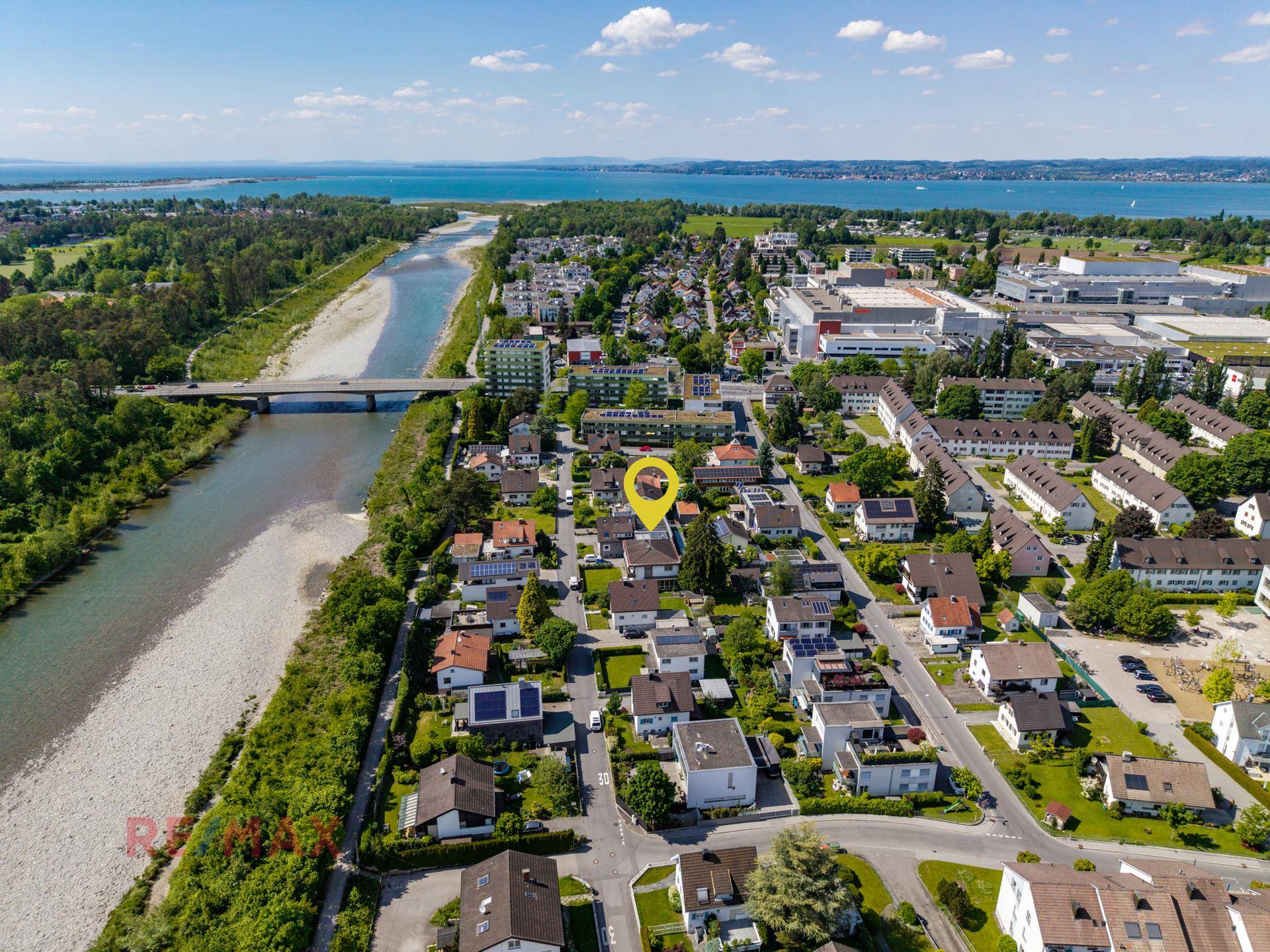 Luftaufnahme einer Wohnsiedlung mit markiertem Grundstück, Fluss und See im Hintergrund.