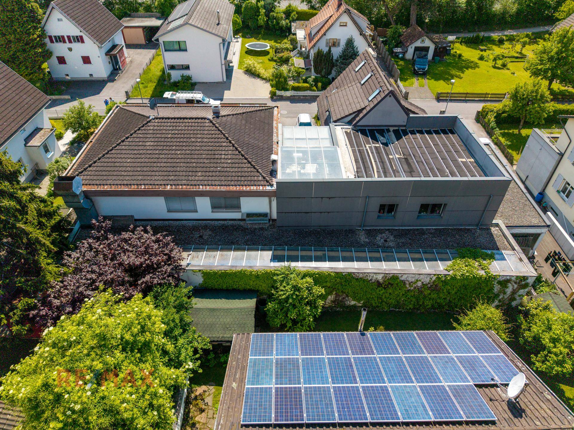 Dachansicht von Wohnhäusern mit Solaranlagen und einem Wintergarten in einer grünen Umgebung.
