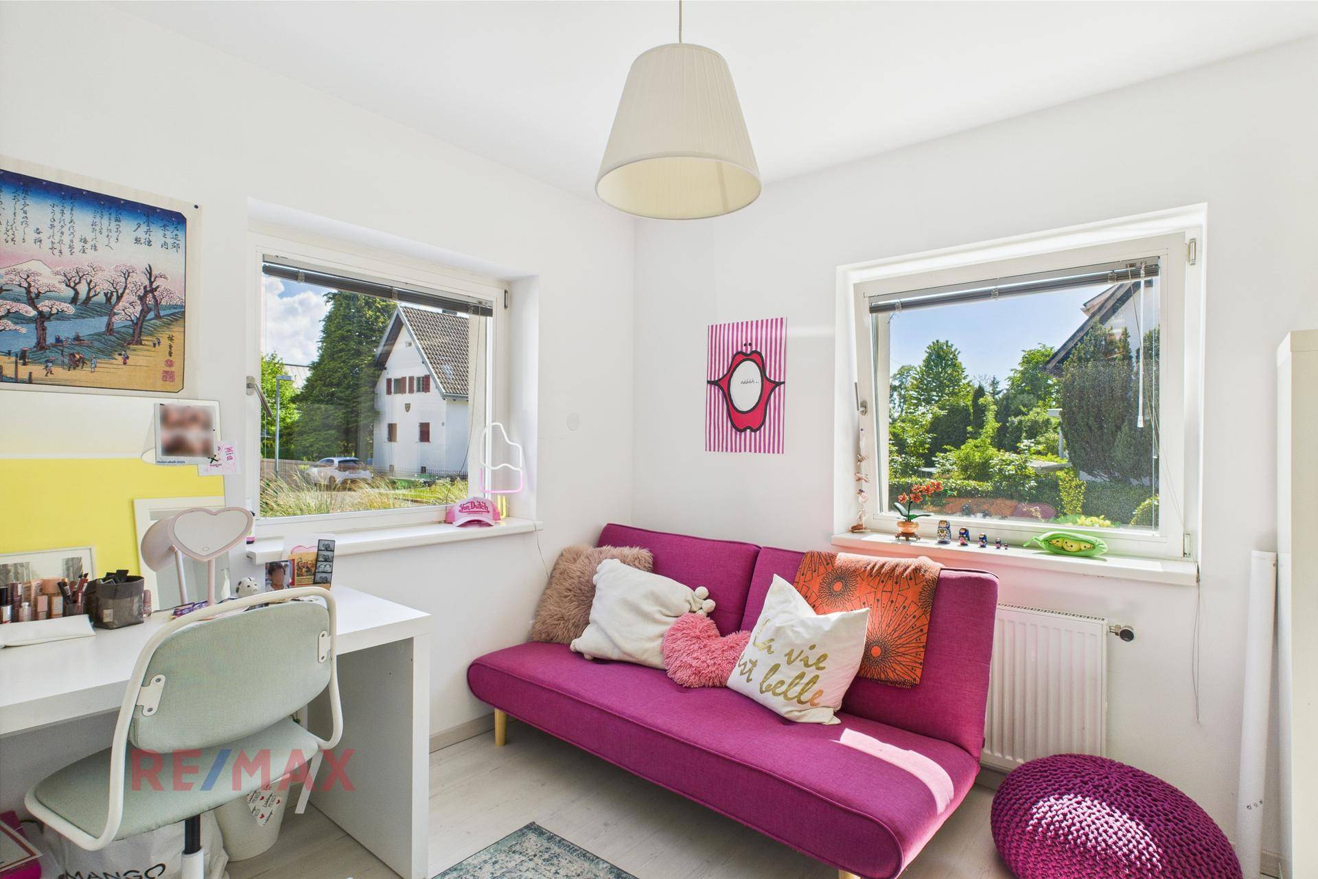 Helles Kinderzimmer mit pinkem Sofa, Schreibtisch und zwei Fenstern mit Blick ins Grüne.