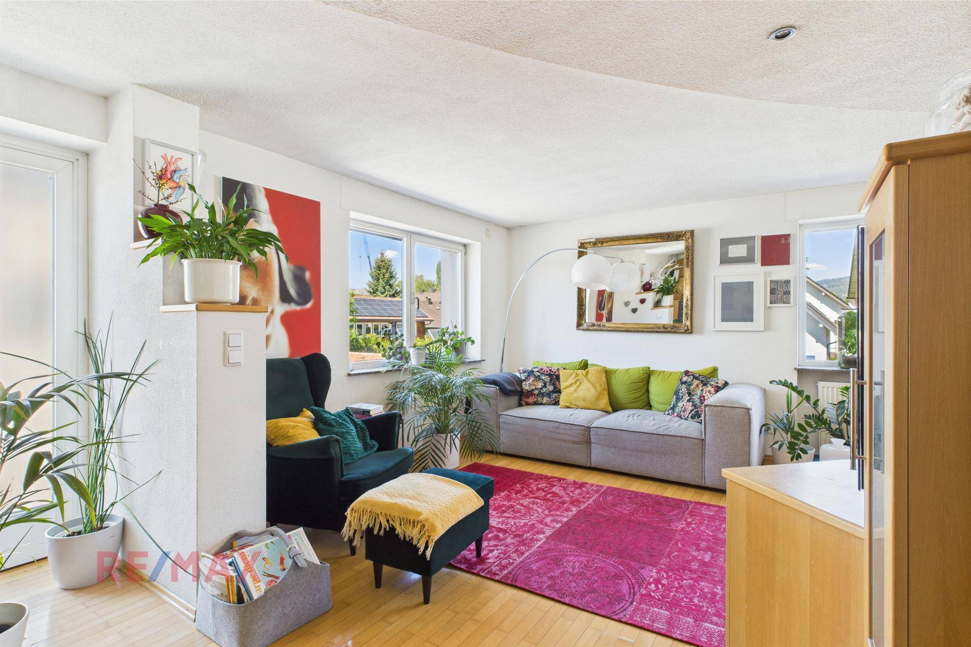 Gemütliches Wohnzimmer mit grauem Sofa, vielen Pflanzen und einem großen Spiegel an der Wand.