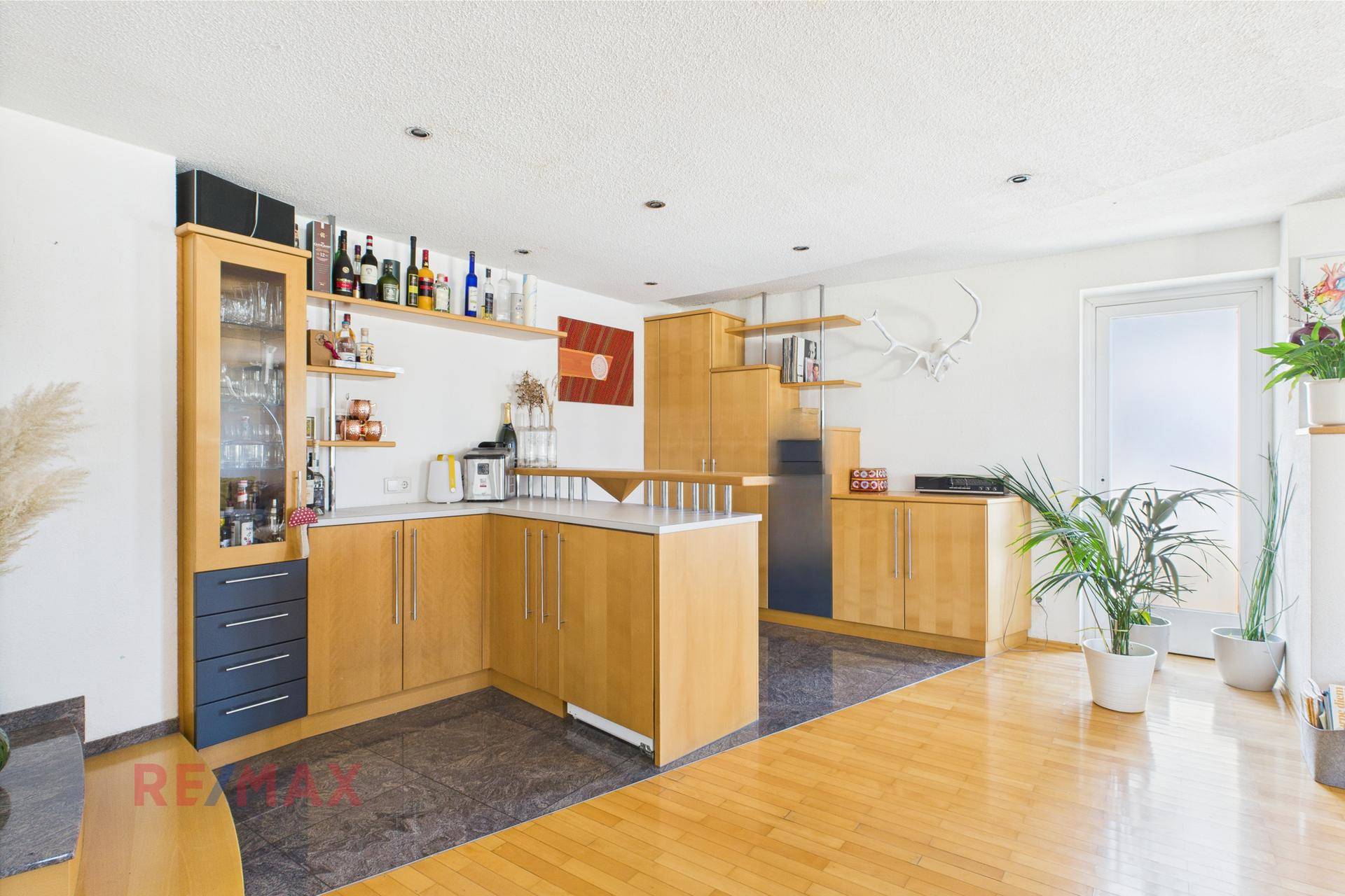 Offene Küche mit Holzschränken, dunklem Fliesenboden und integrierten Regalen für Flaschen und Gläser.
