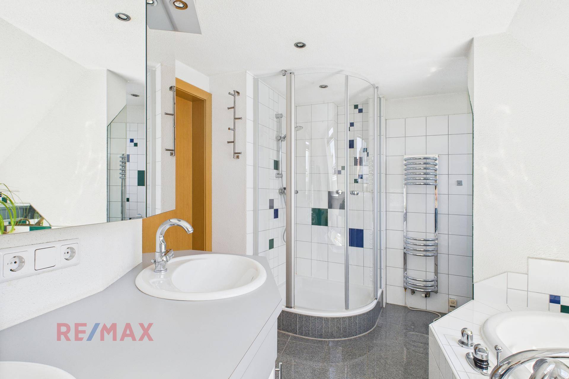 Badezimmer mit Duschkabine, Doppelwaschbecken und beheiztem Handtuchhalter an der Wand.